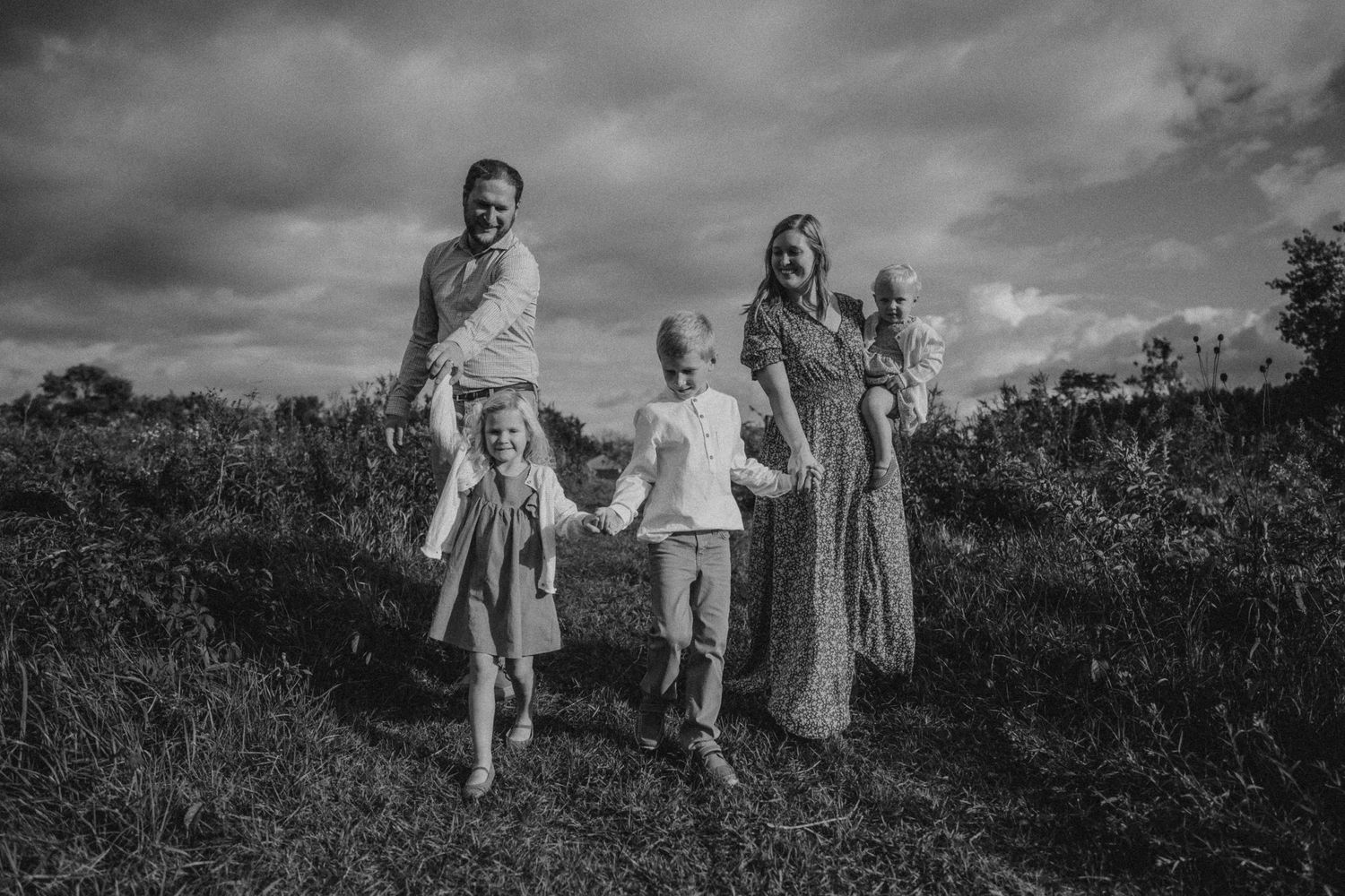 A joyful black and white portrait of a family running together on a grassy hillside.