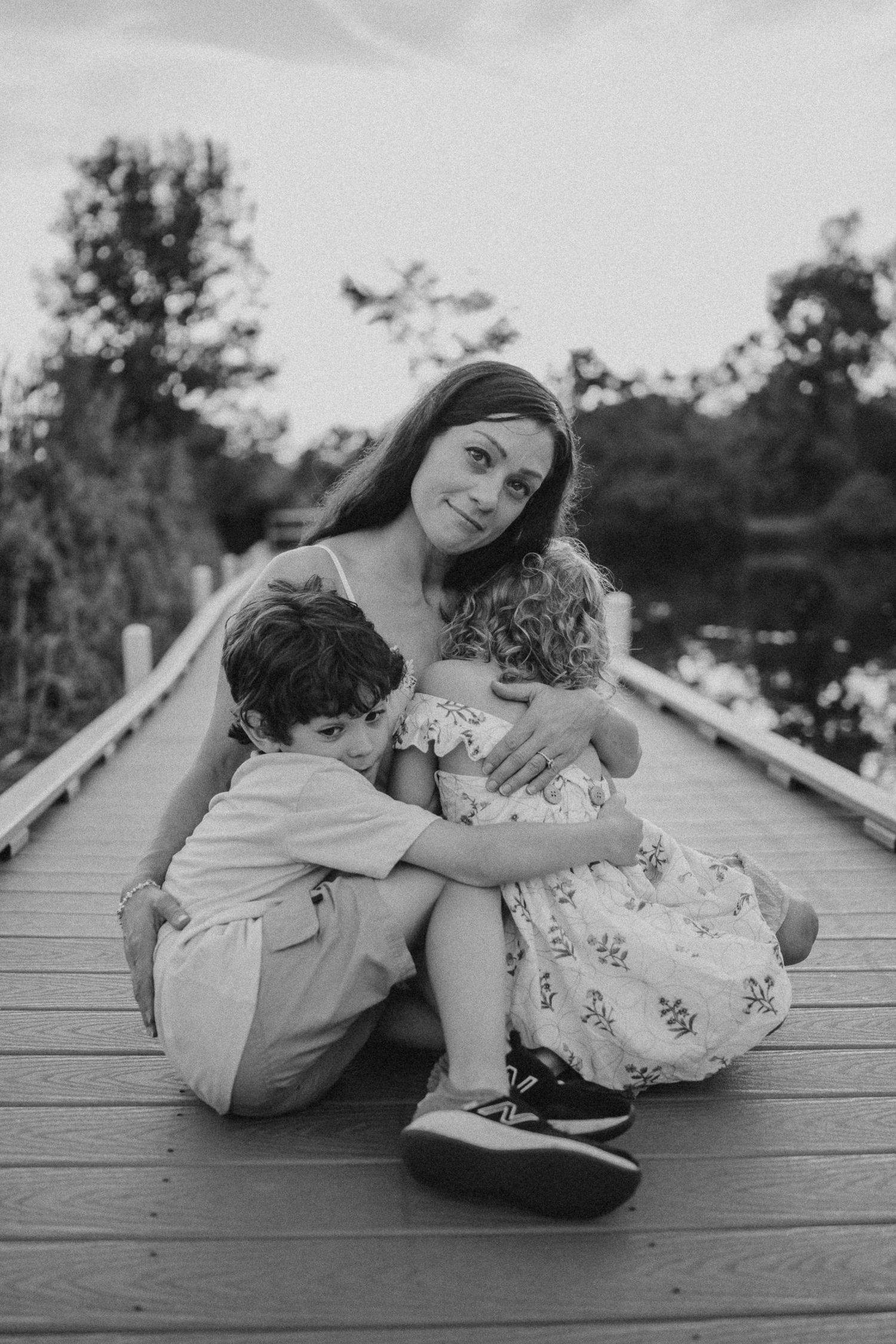 A tender family embrace captured in black and white on a wooden boardwalk.