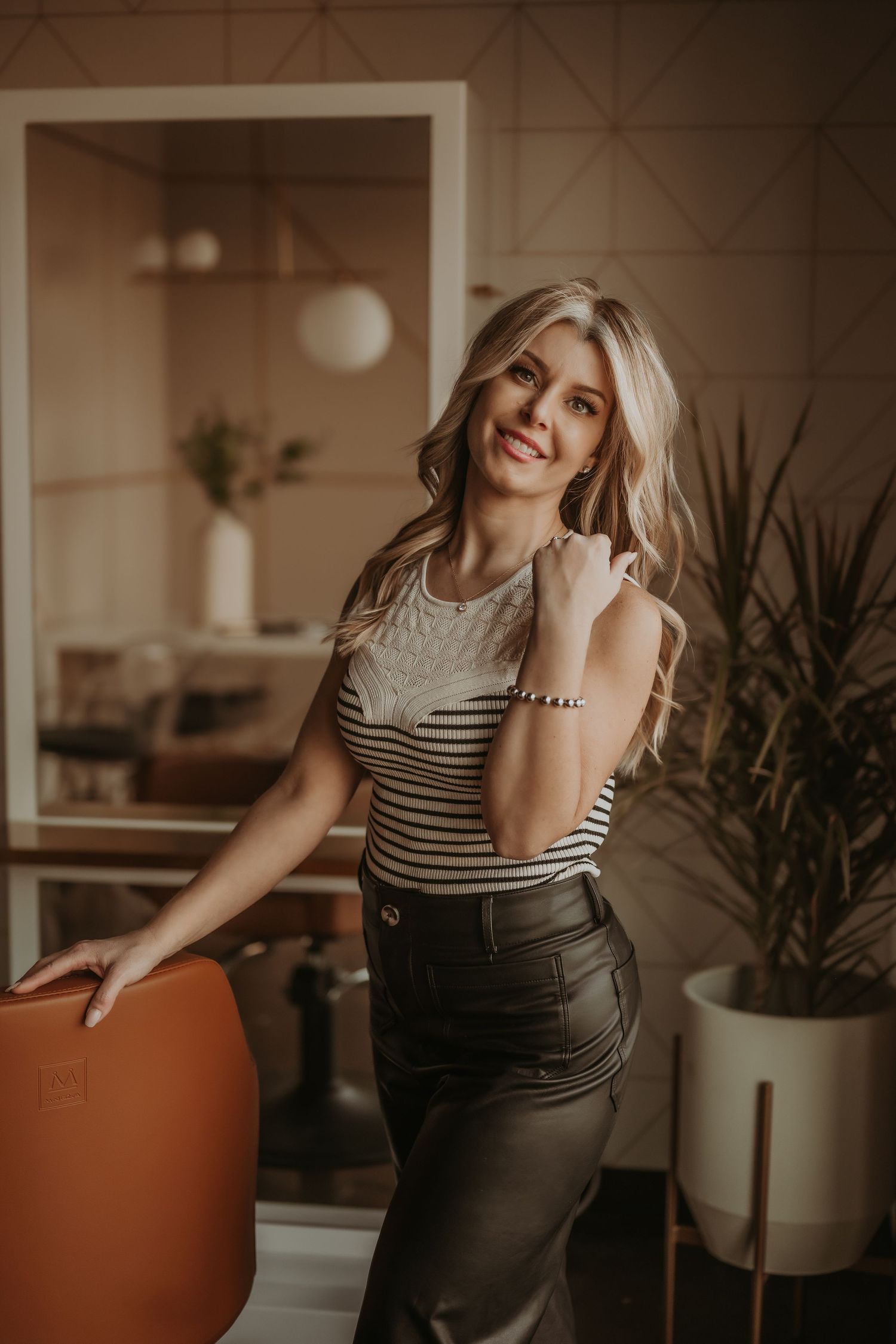 Professional interior portrait showing a striped top and dark pants against a warm-toned modern office setting with plants.