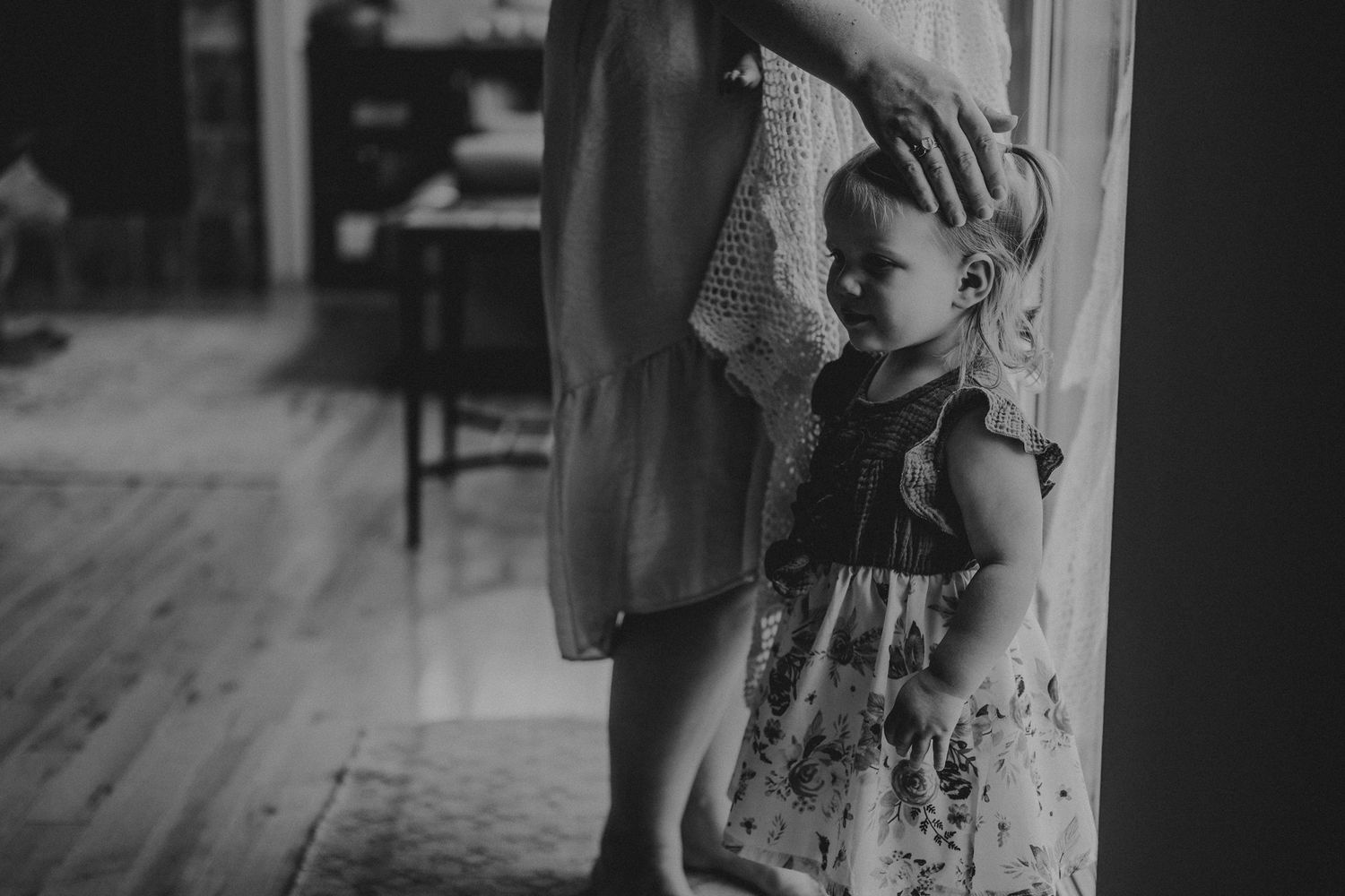 Black and white portrait capturing tender moment between parent and child by window.