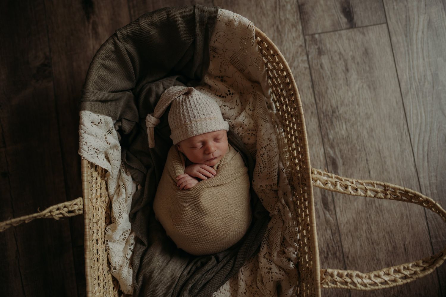 Overhead view of sleeping newborn in tan swaddle blanket resting in woven basket.