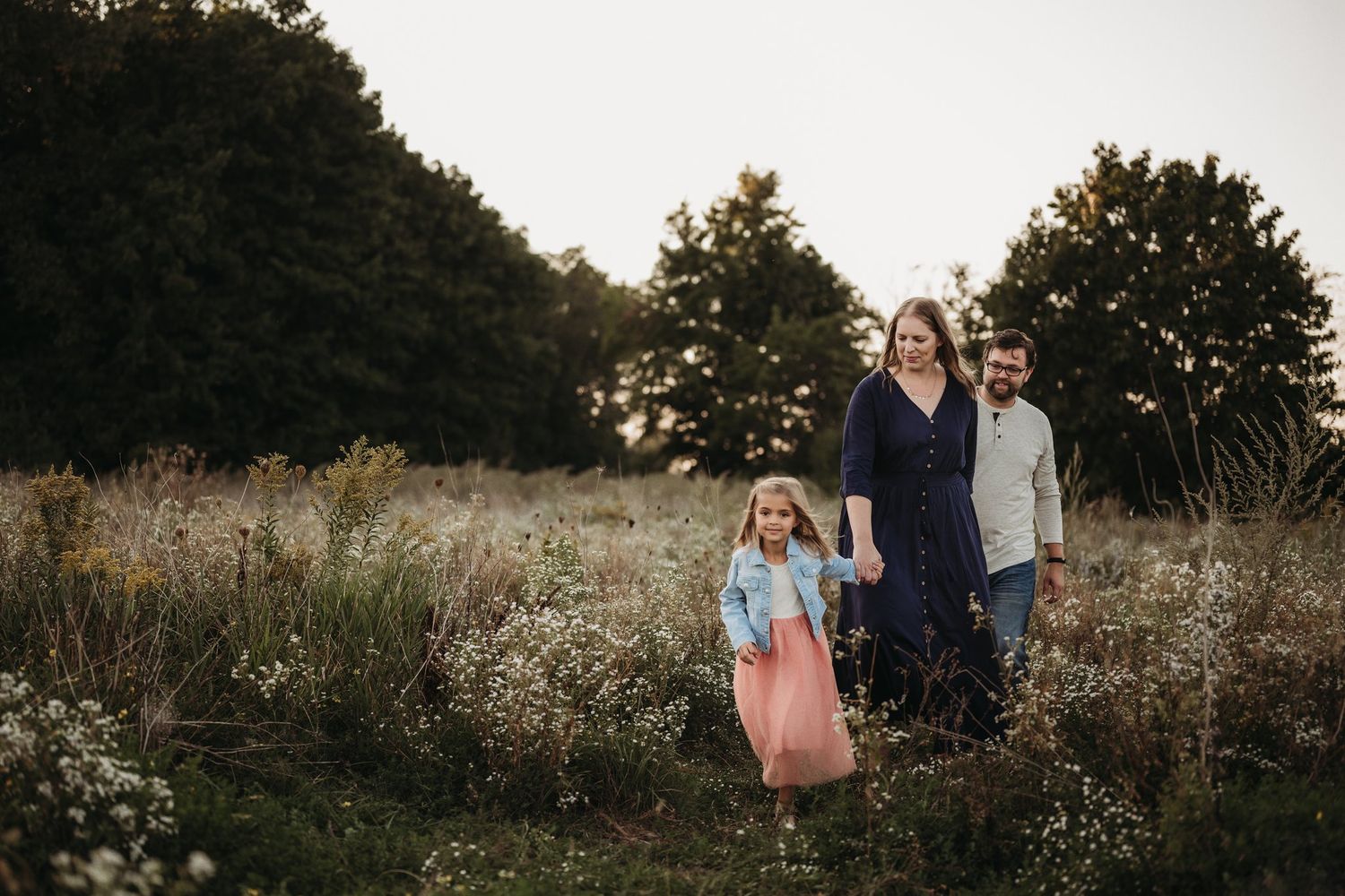 Family stands together in golden evening light among wildflowers and tall grass.
