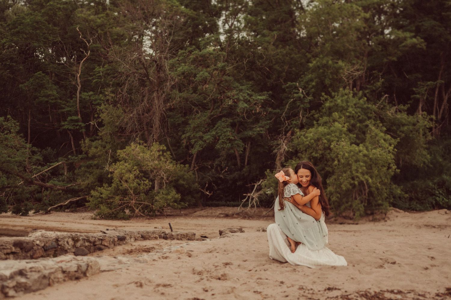 A tender embrace shared on a sandy beach with lush trees in the background.