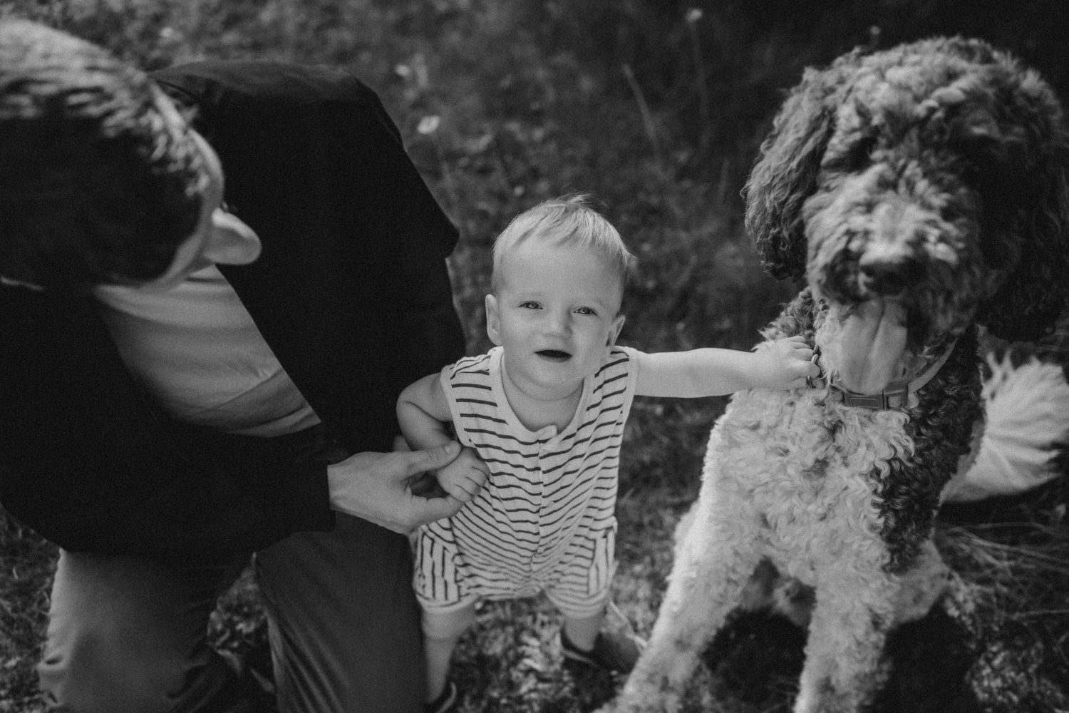 A black and white photo showing a family and their curly-haired dog outdoors.