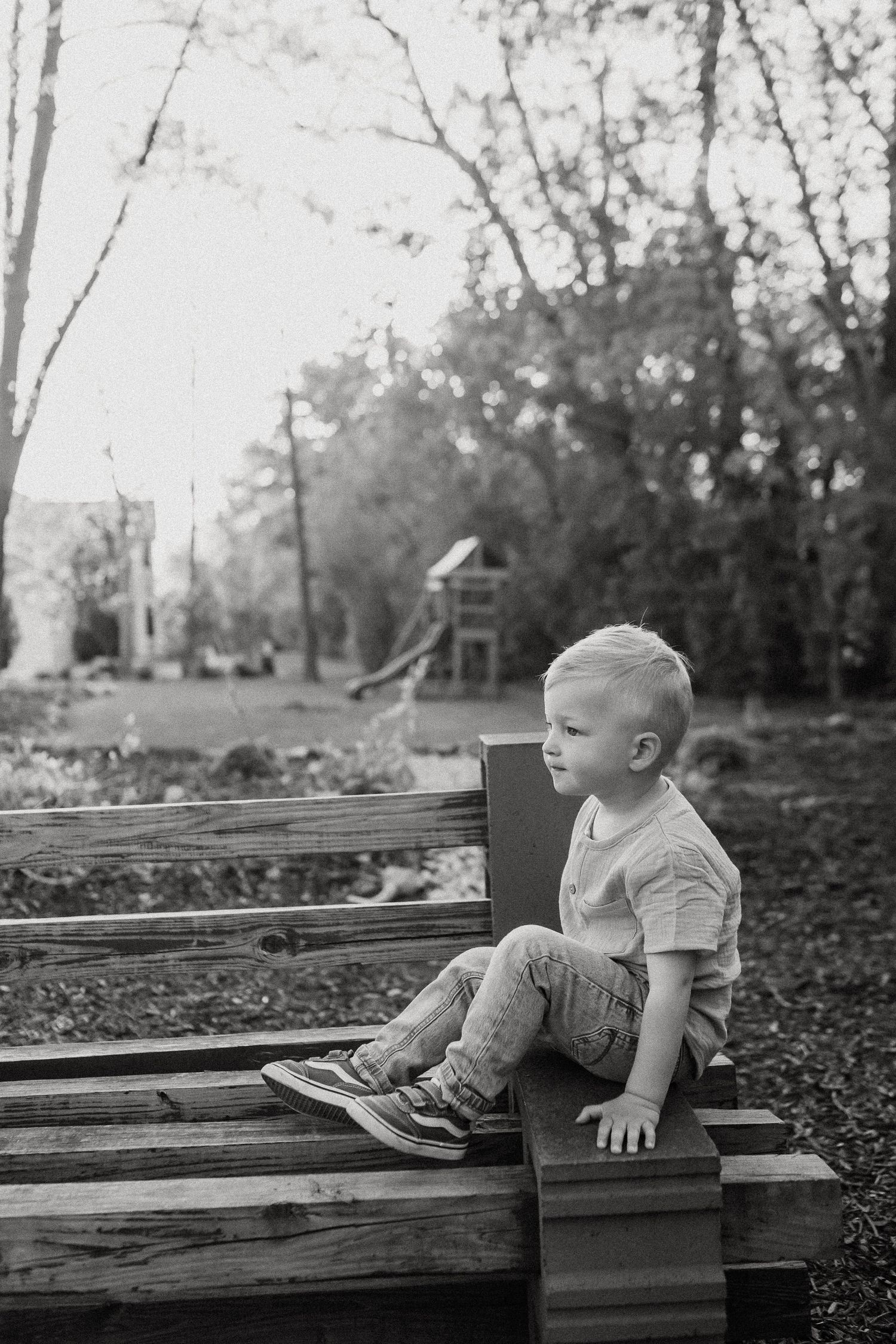 Black and white photo of a young boy sitting alone on wooden steps in a park setting.