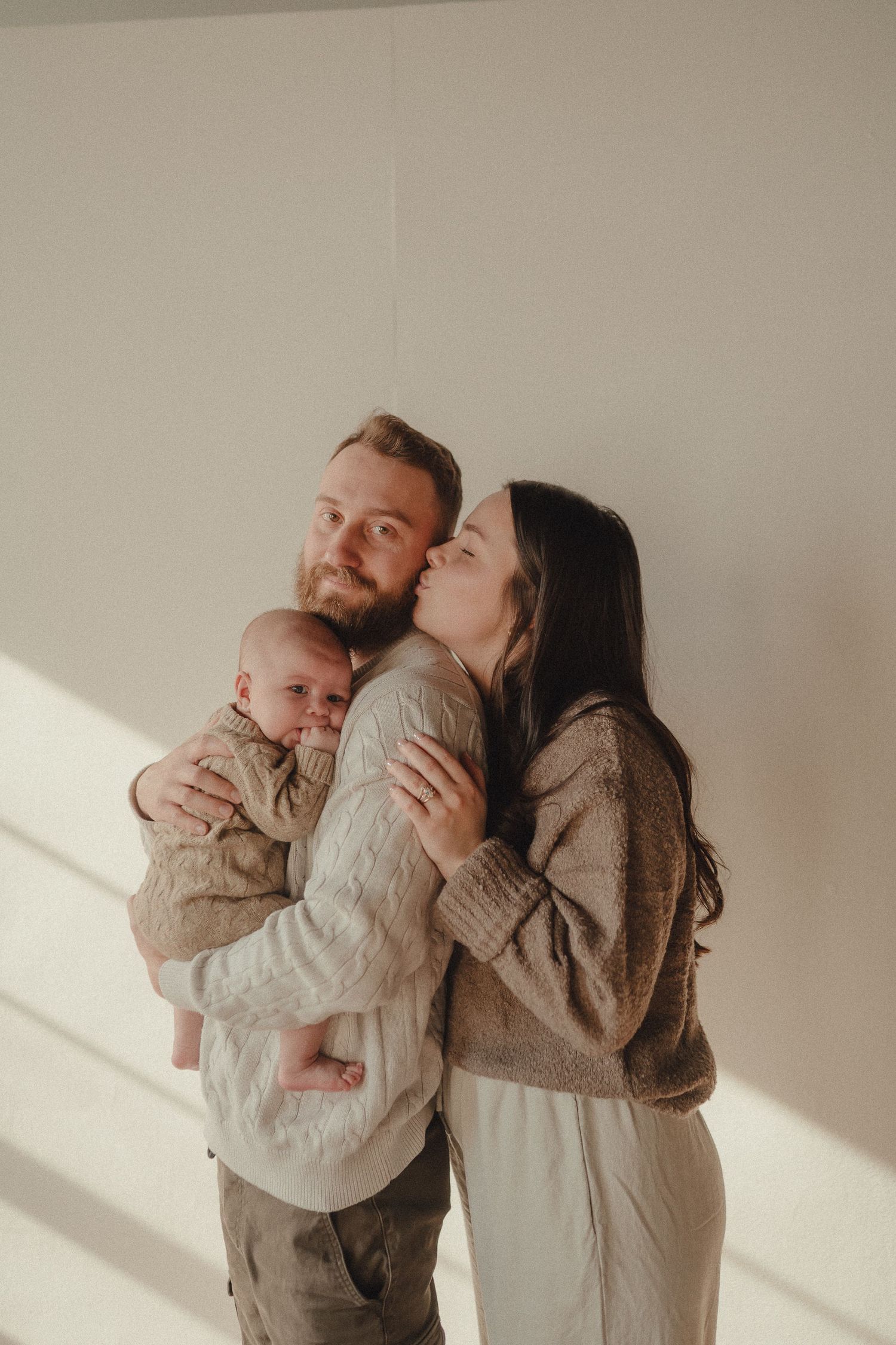 Natural light studio portraits showing tender family interactions in neutral colored clothing.