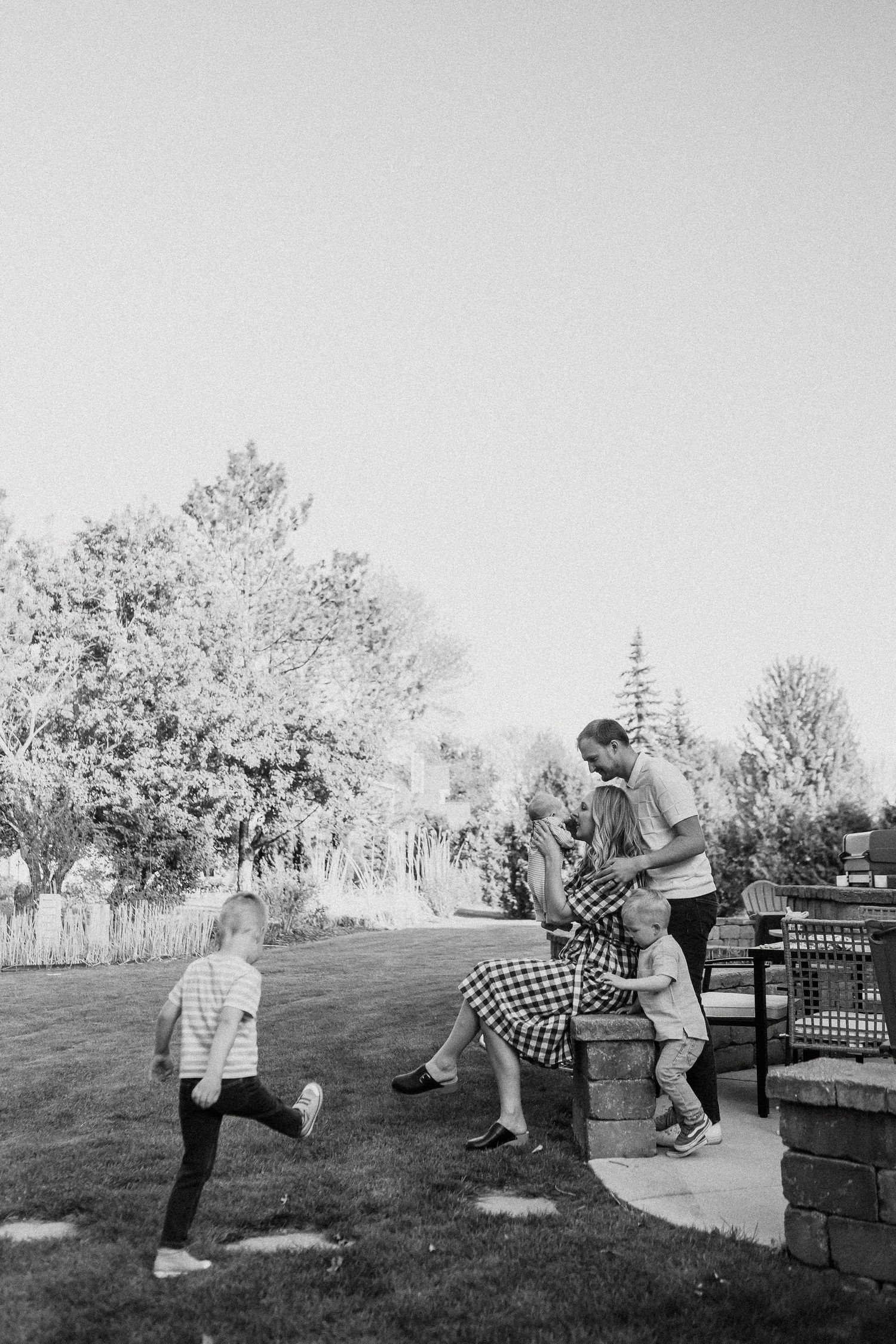 Black and white photo of a family relaxing in a backyard while a child runs across the lawn.