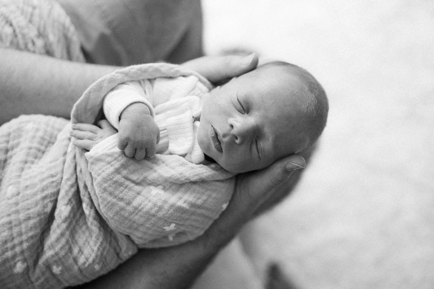 Newborn baby sleeping peacefully in soft white swaddling blanket.