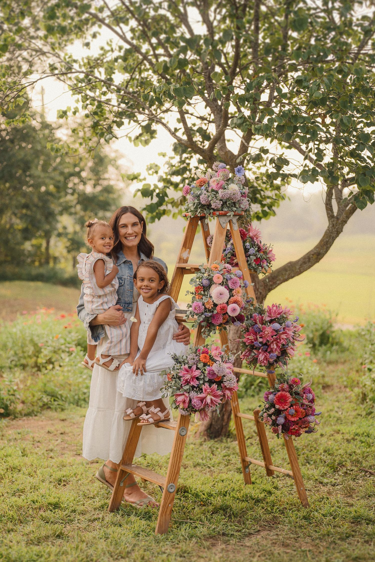 A sweet family photo by a wooden ladder adorned with cascading pink and purple flowers in a sunny garden setting.