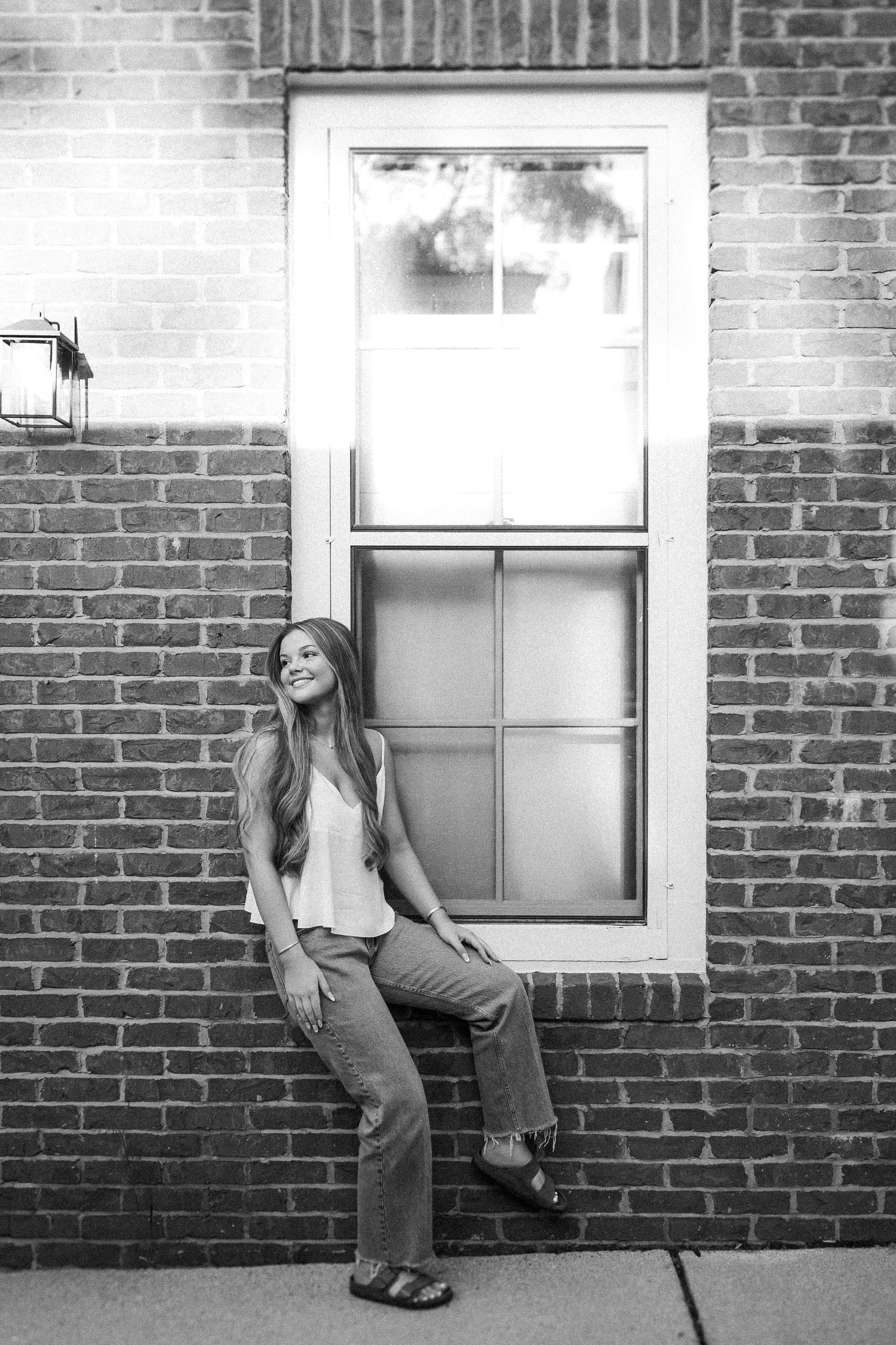 Black and white portrait against brick wall with window, casual outfit and relaxed pose.
