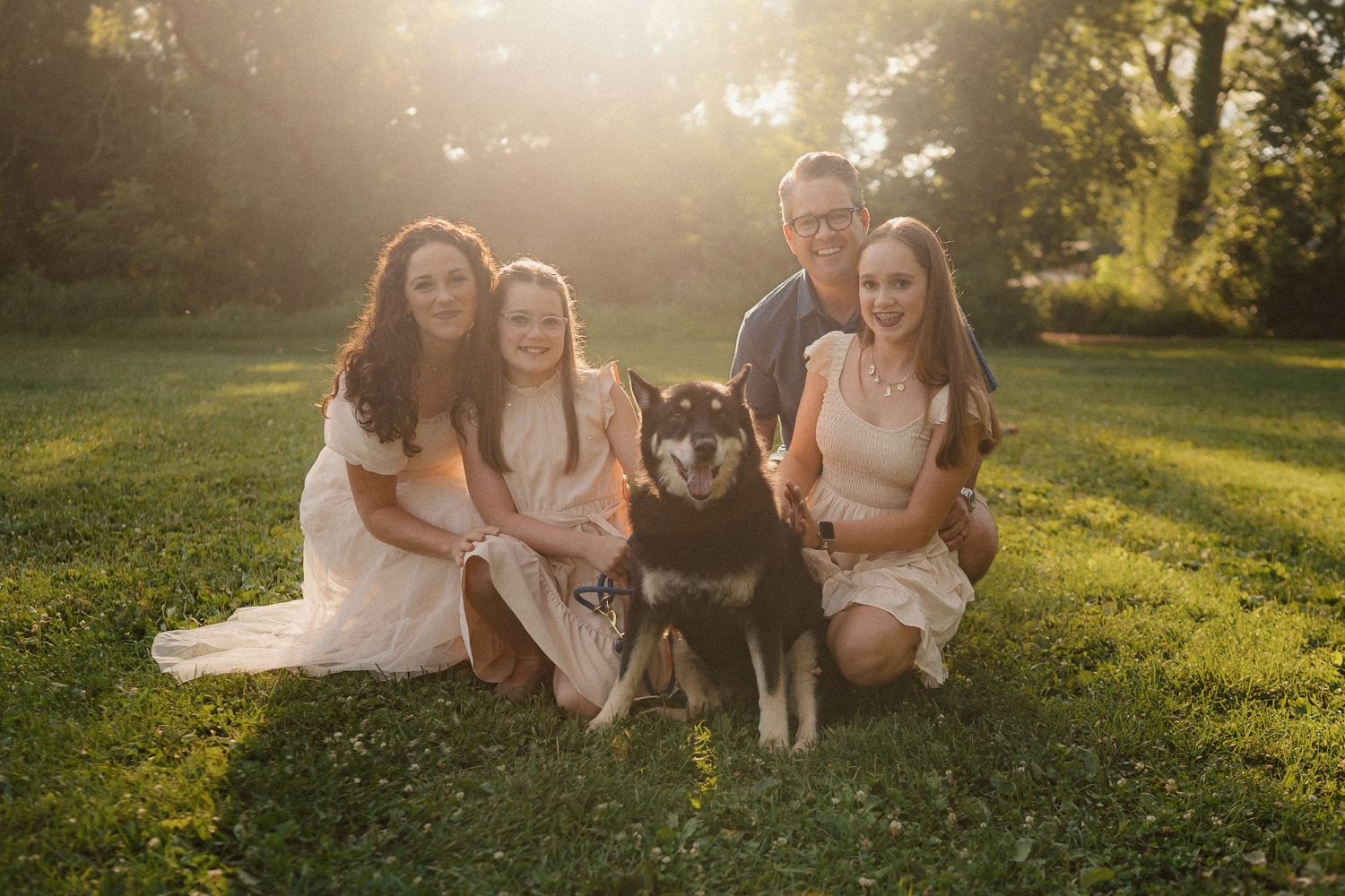 A family poses with their black and tan dog on a sunny lawn during a golden hour photoshoot.
