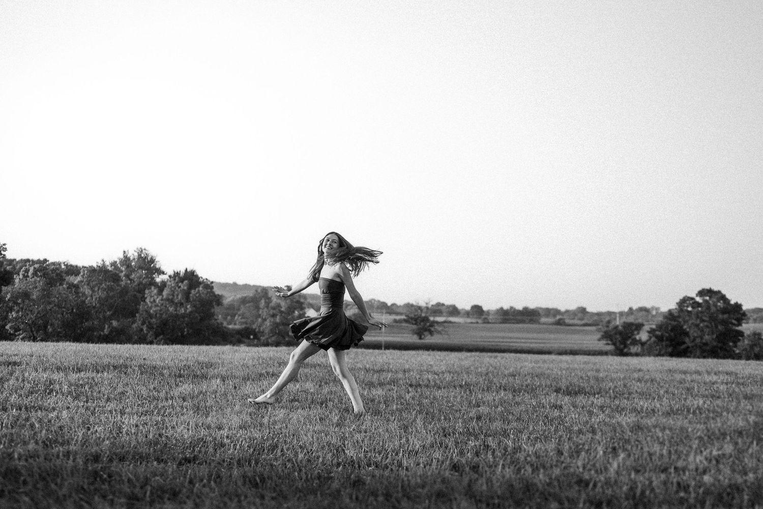 Black and white silhouette of someone joyfully leaping across an open field at sunset.