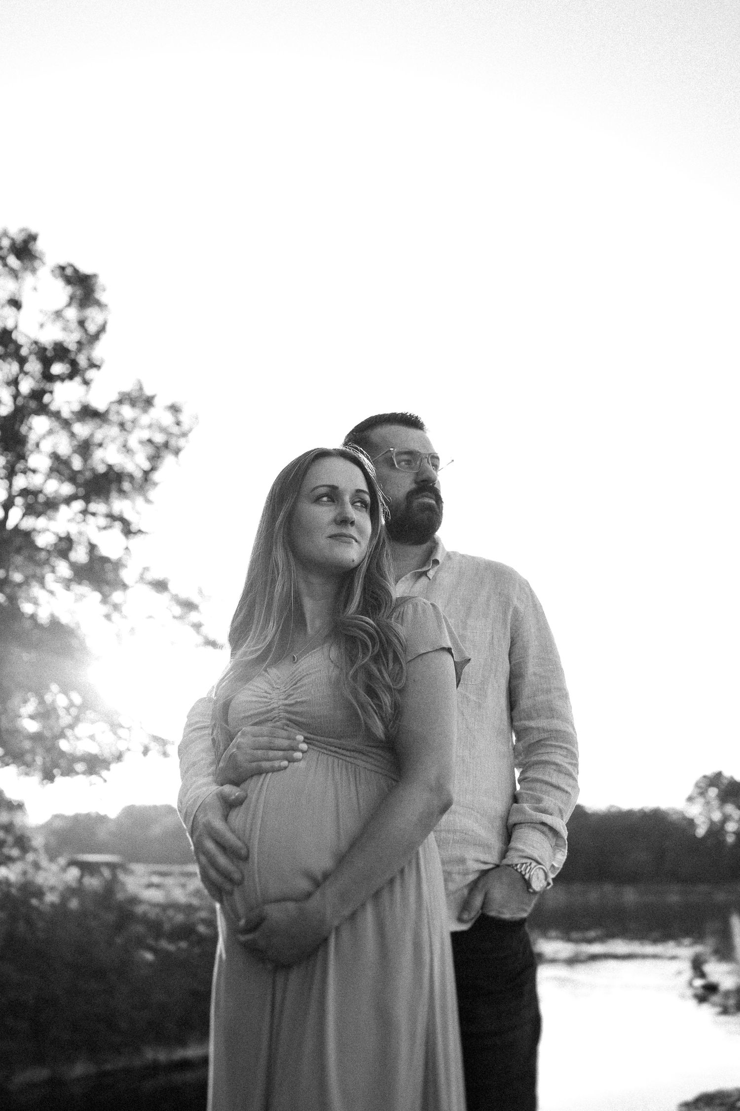 A couple shares an intimate moment while standing near a lake at sunset.