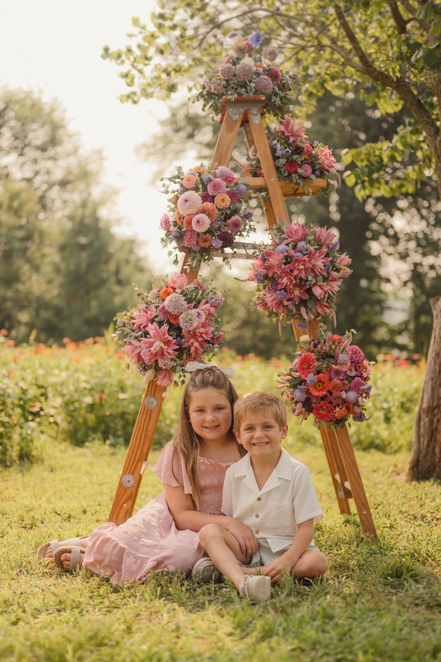 Two figures lounge together on grass under floral arches during a golden hour outdoor photo session.