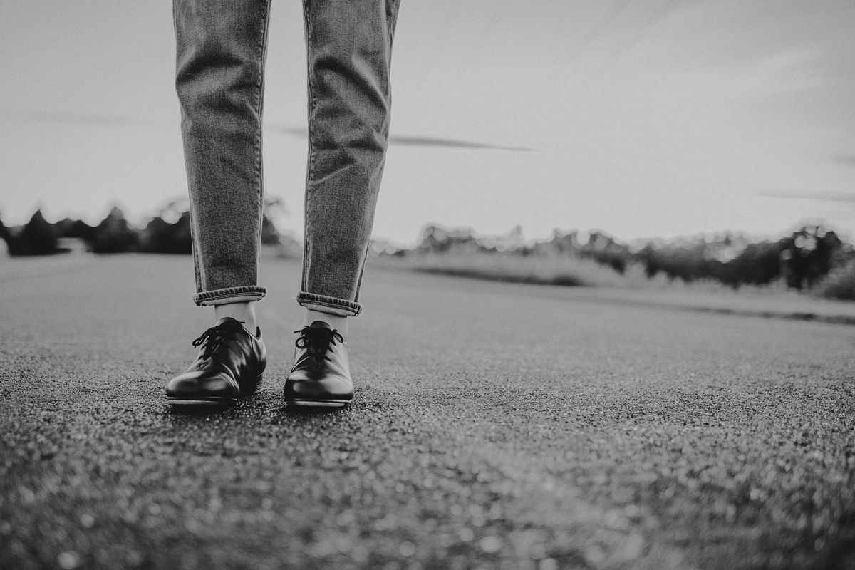 Black and white photo of legs wearing jeans and sneakers standing on textured ground.