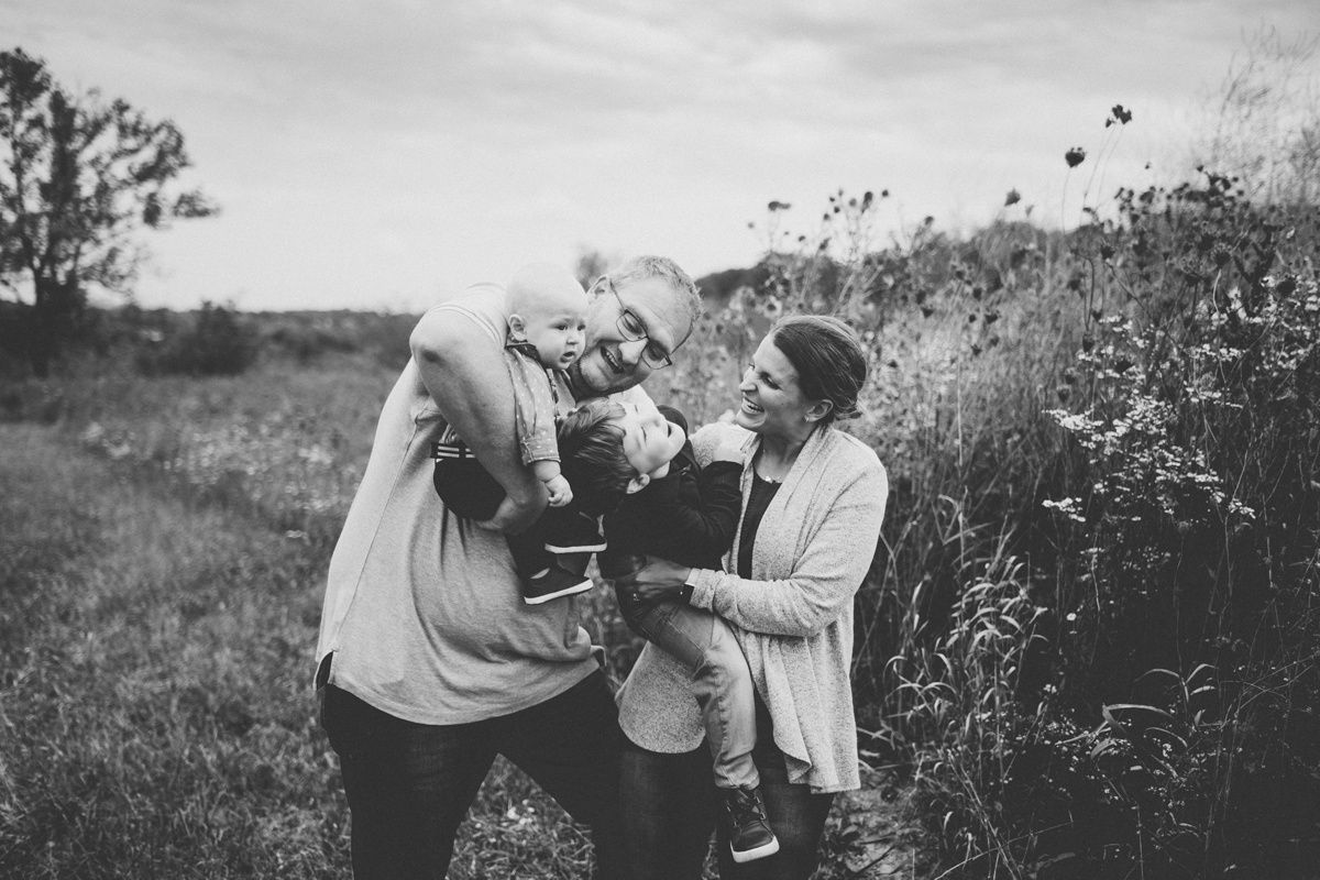 Black and white candid image of family sharing tender moment in wildflower field.
