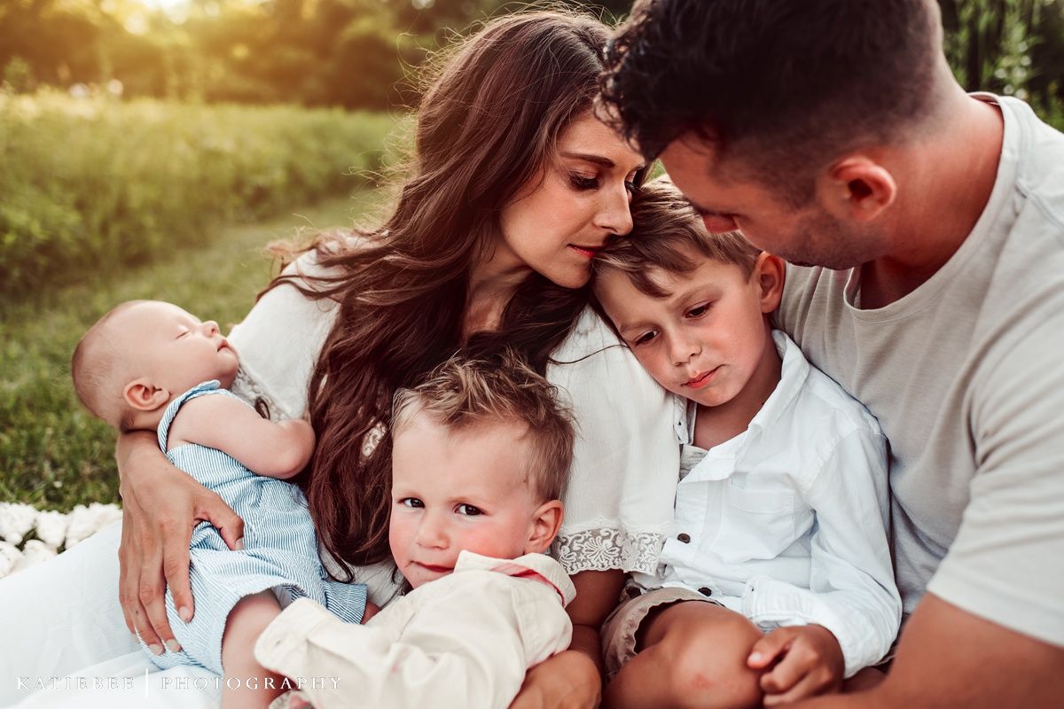 Intimate outdoor family portrait on white blanket during golden hour sunset in grassy field.