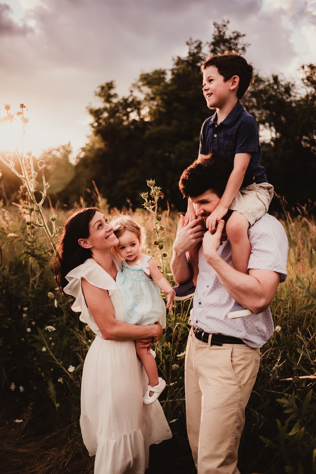 Family playing and laughing together in tall grass during golden hour.