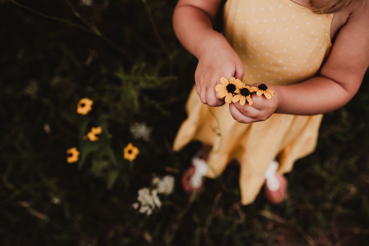 Close-up view of hands holding wildflowers against a yellow dress.
