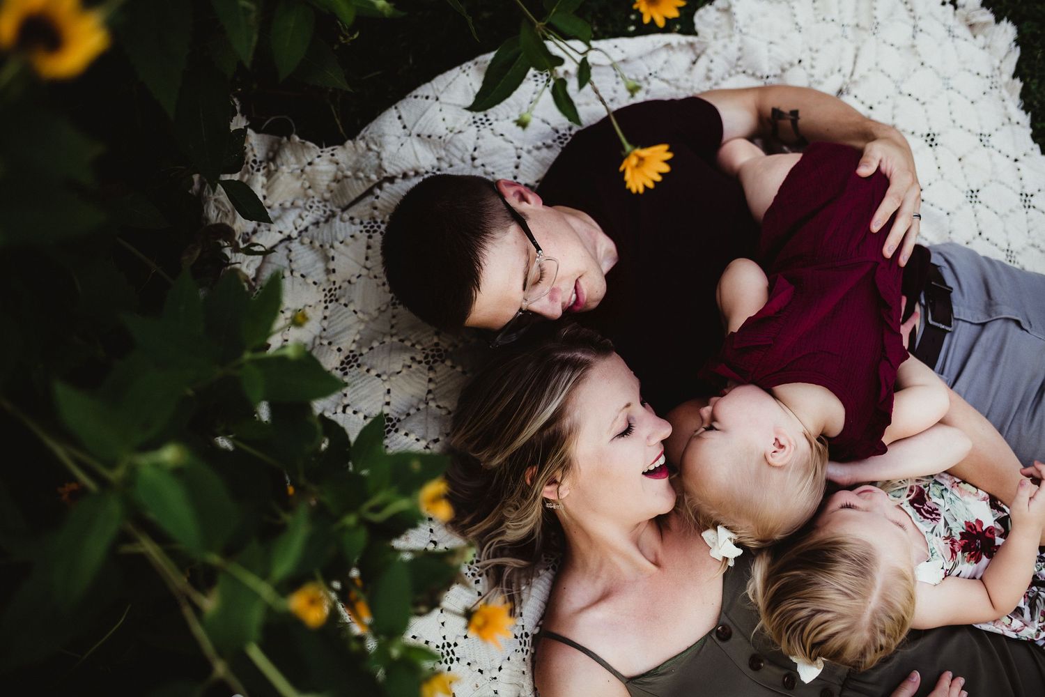 Candid portrait of loved ones lying together on a blanket surrounded by yellow flowers.