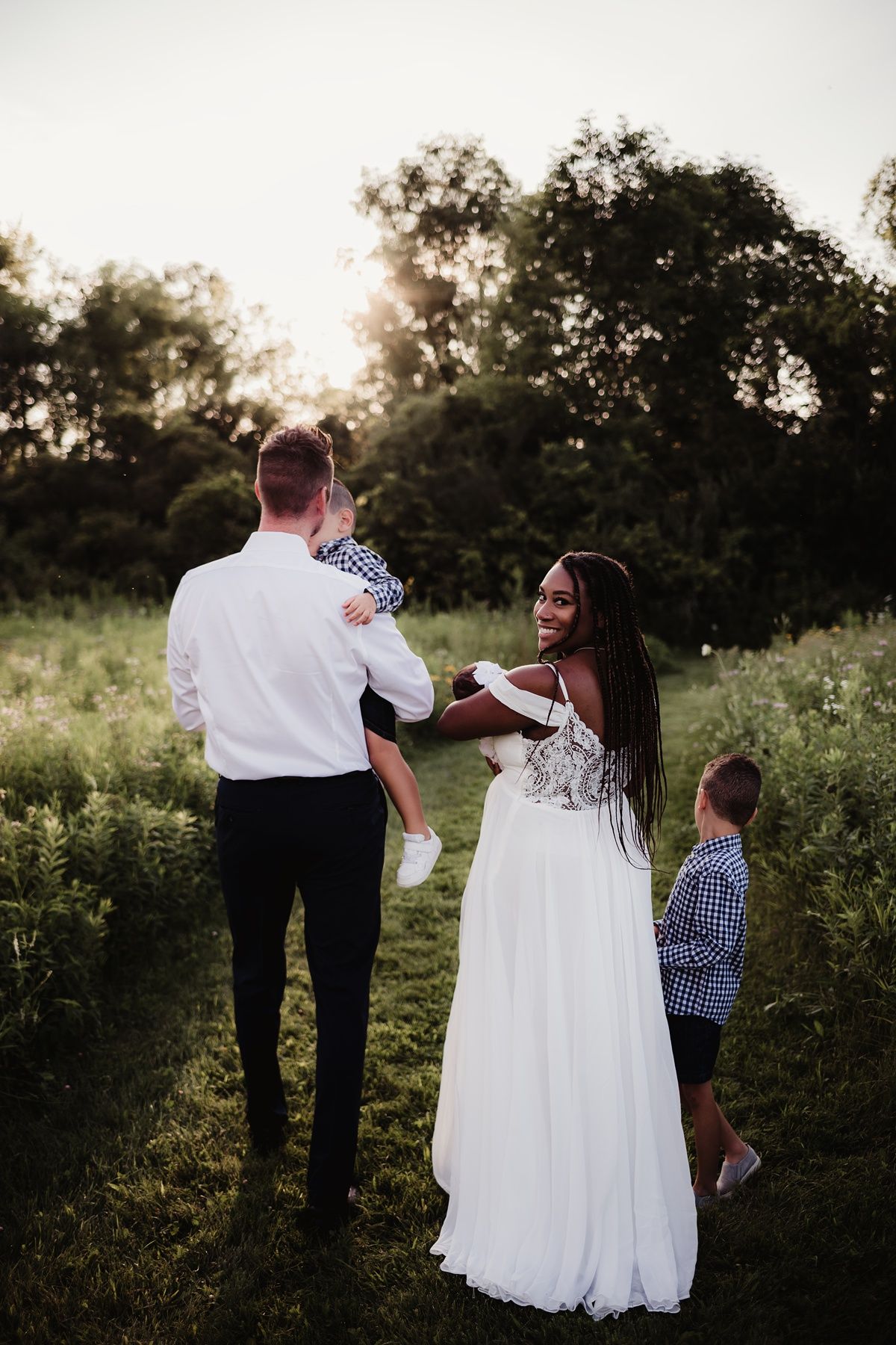 Wedding party gathered in golden hour sunlight among tall grasses.