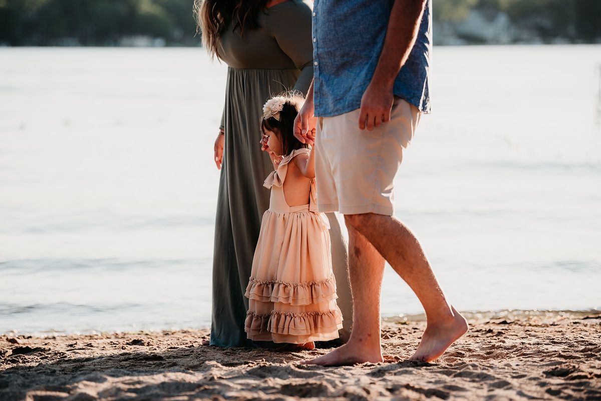 A tender family moment captured at the beach with flowing dresses and bare feet in the sand.