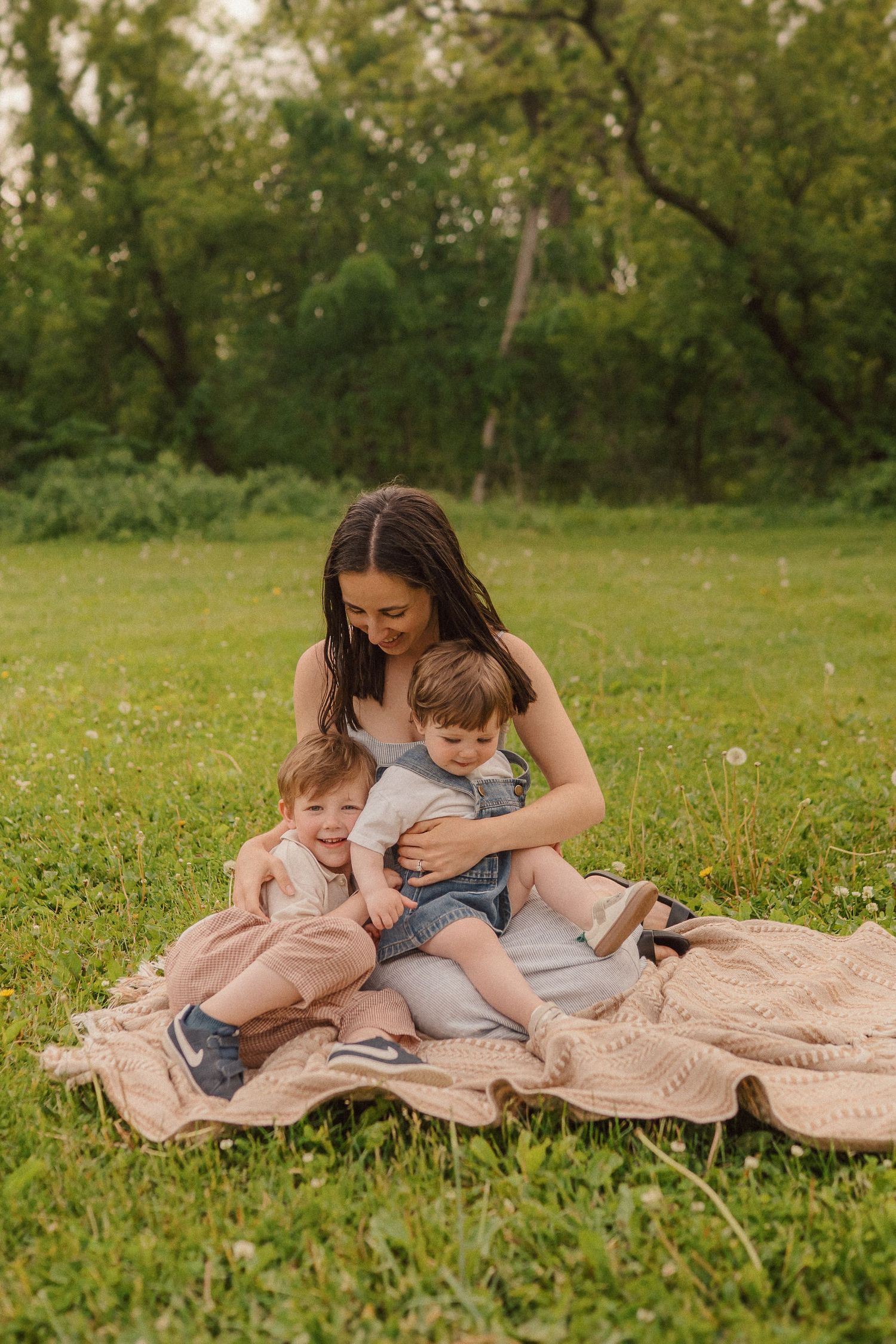 A parent and children share tender moments while relaxing on a blanket in a sunny meadow full of wildflowers.