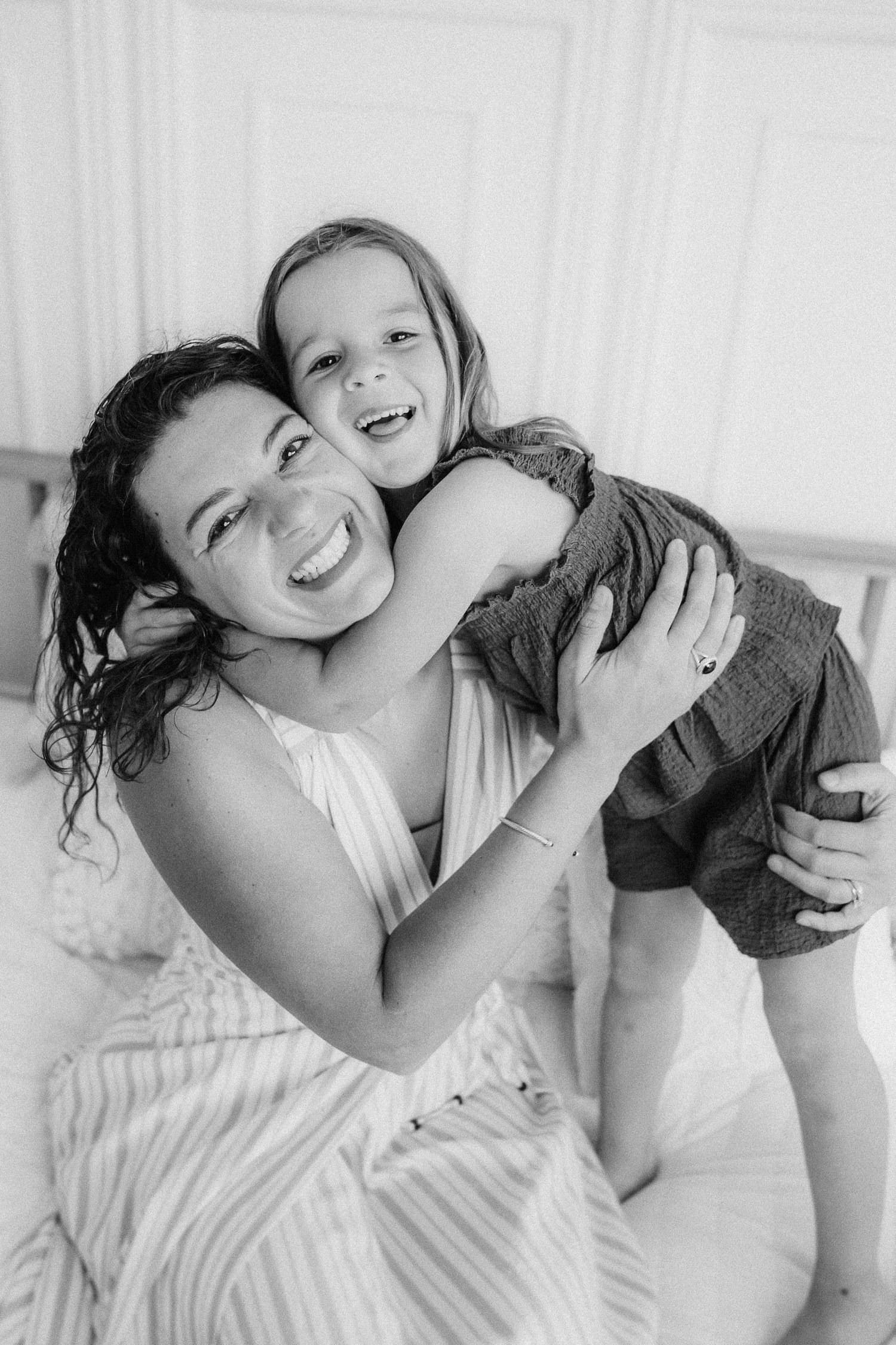 Black and white portrait capturing joyful candid moment on white bed.