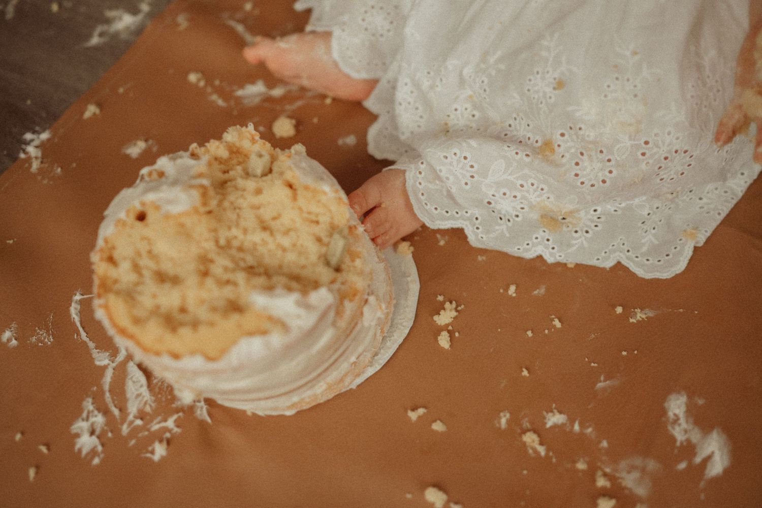 Close-up of a smashed white cake with frosting scattered on an orange surface.