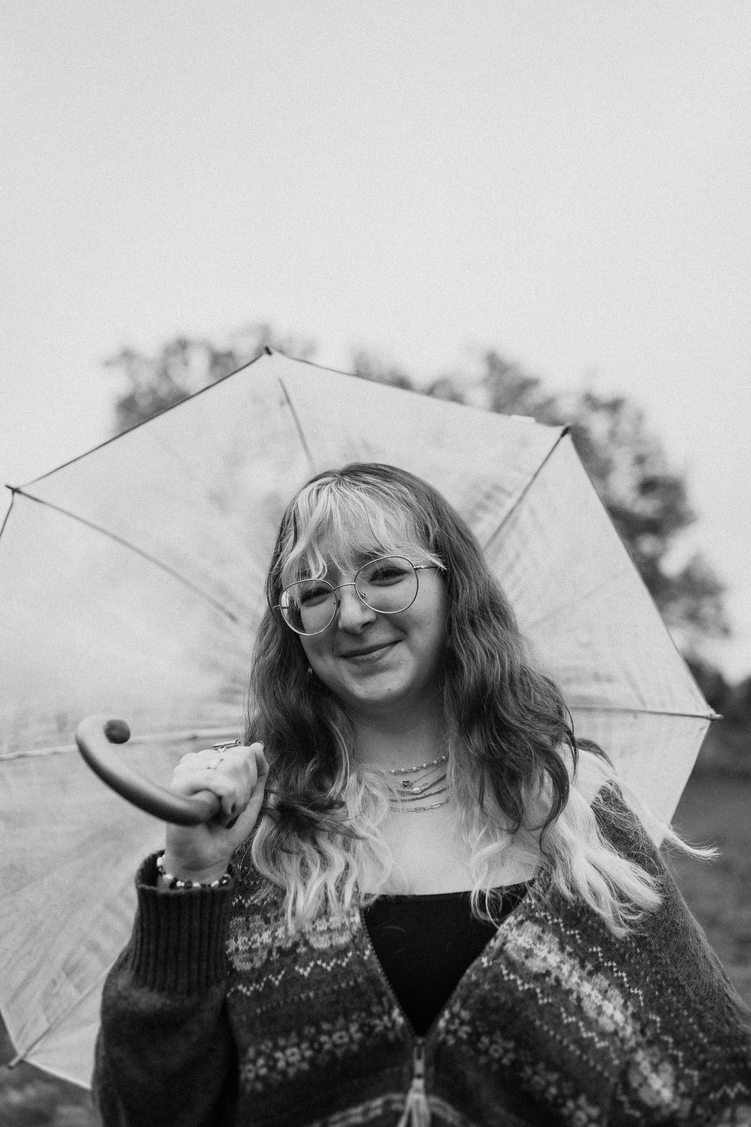 A cheerful black and white portrait under a clear umbrella featuring a patterned knit sweater.