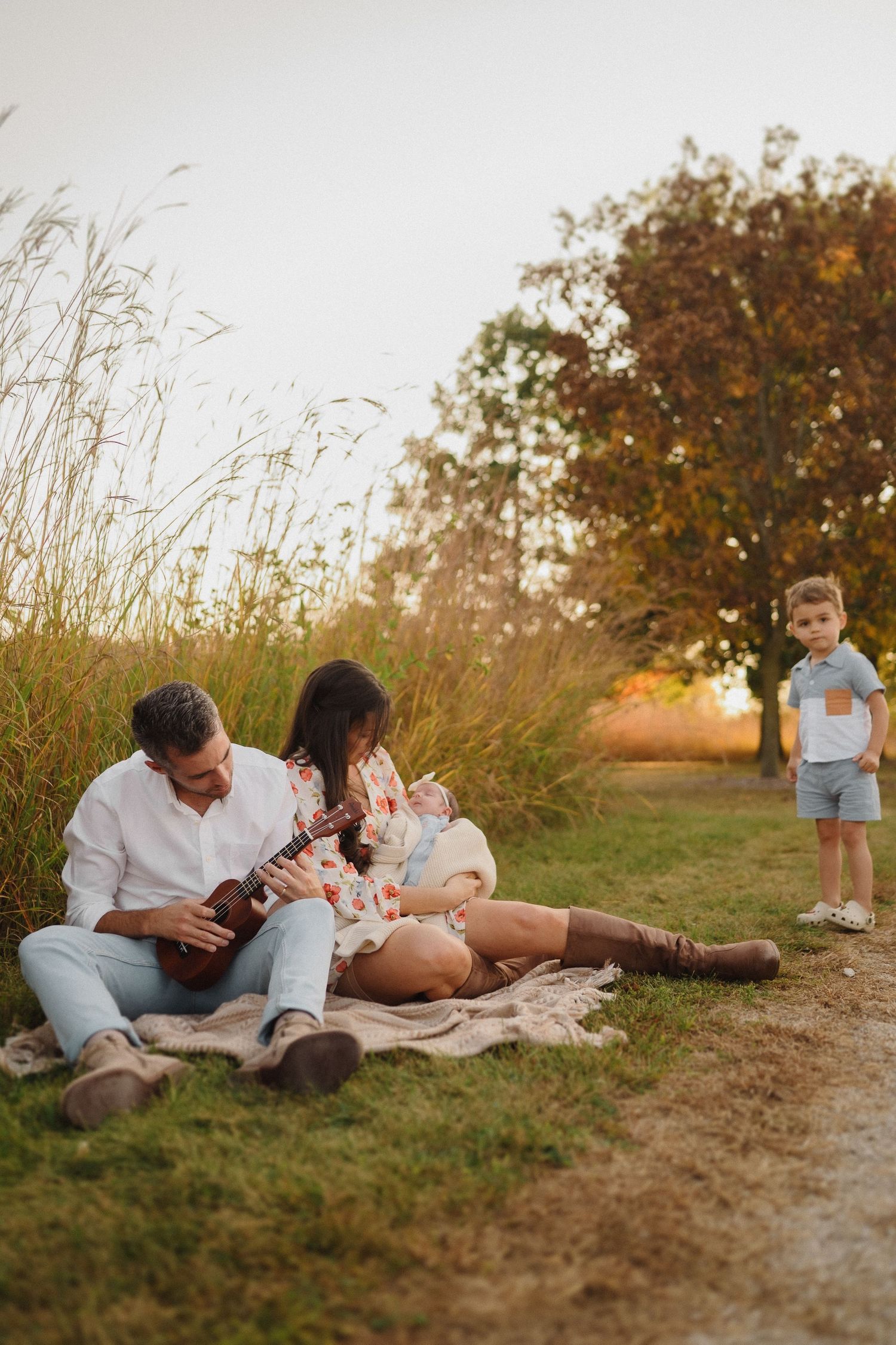 Family having a picnic while someone plays ukulele near autumn trees at golden hour.