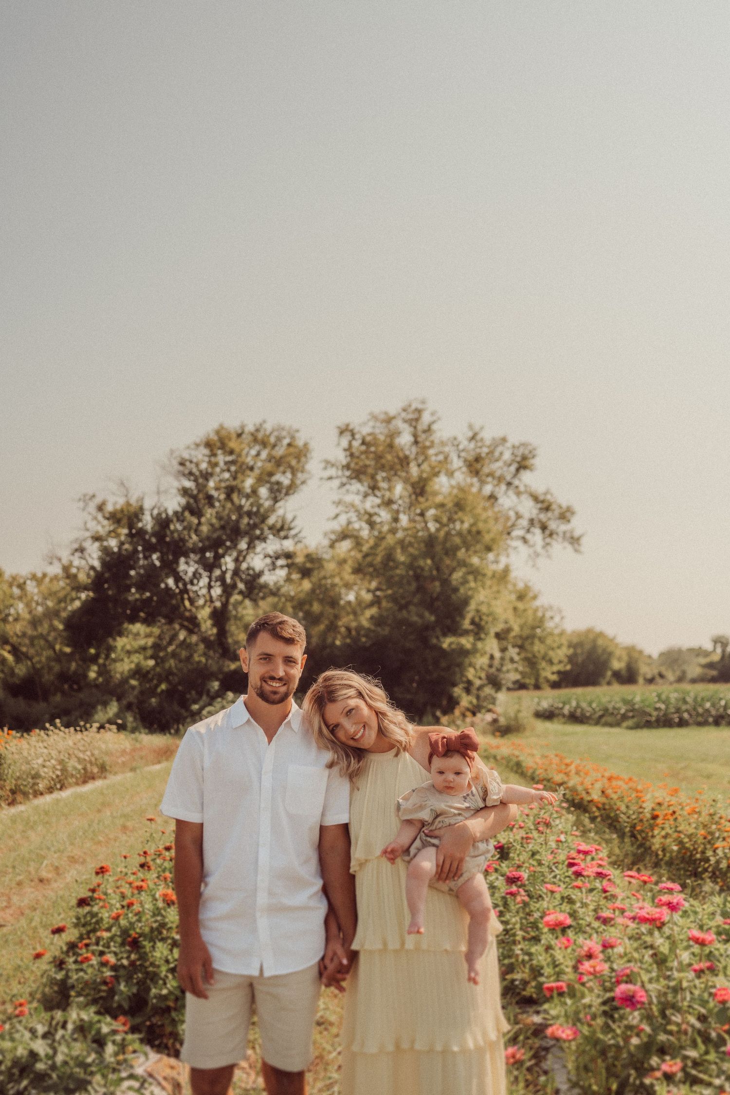 Family poses together in a dreamy flower garden setting with warm sunset lighting.