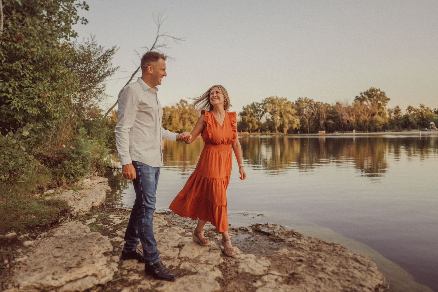Couple walking along lakeside path during golden hour.