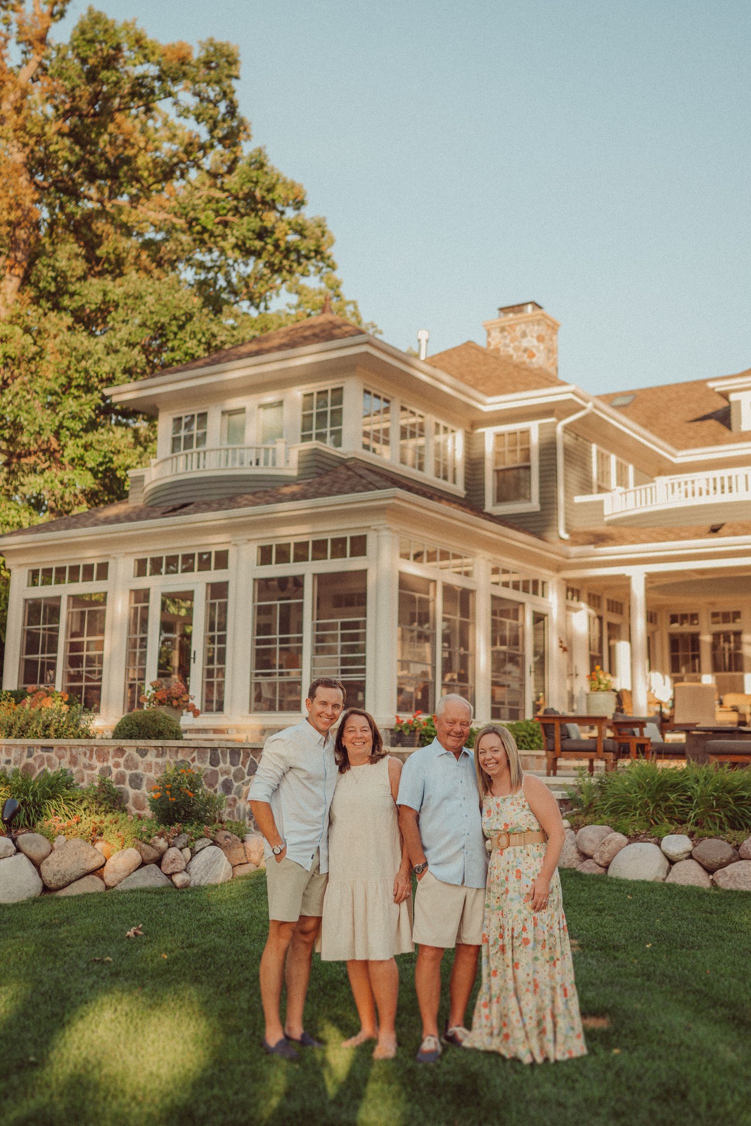 Family group poses together in front of a grand waterfront estate with stone landscaping.