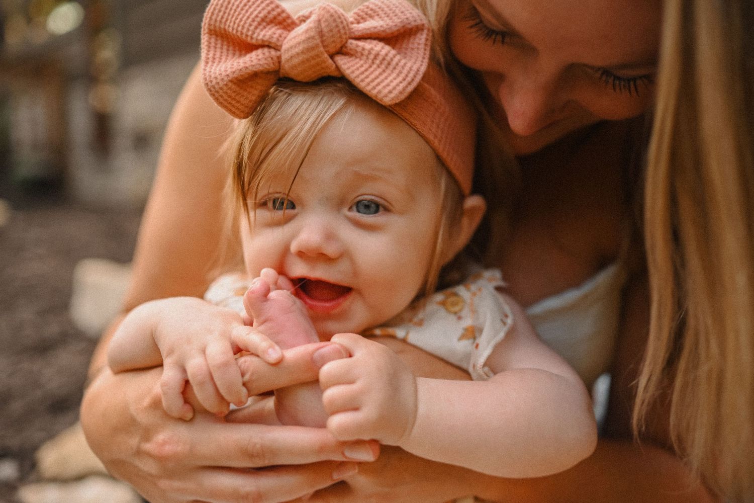 A sweet moment captured of a baby wearing a peach bow and white dress.