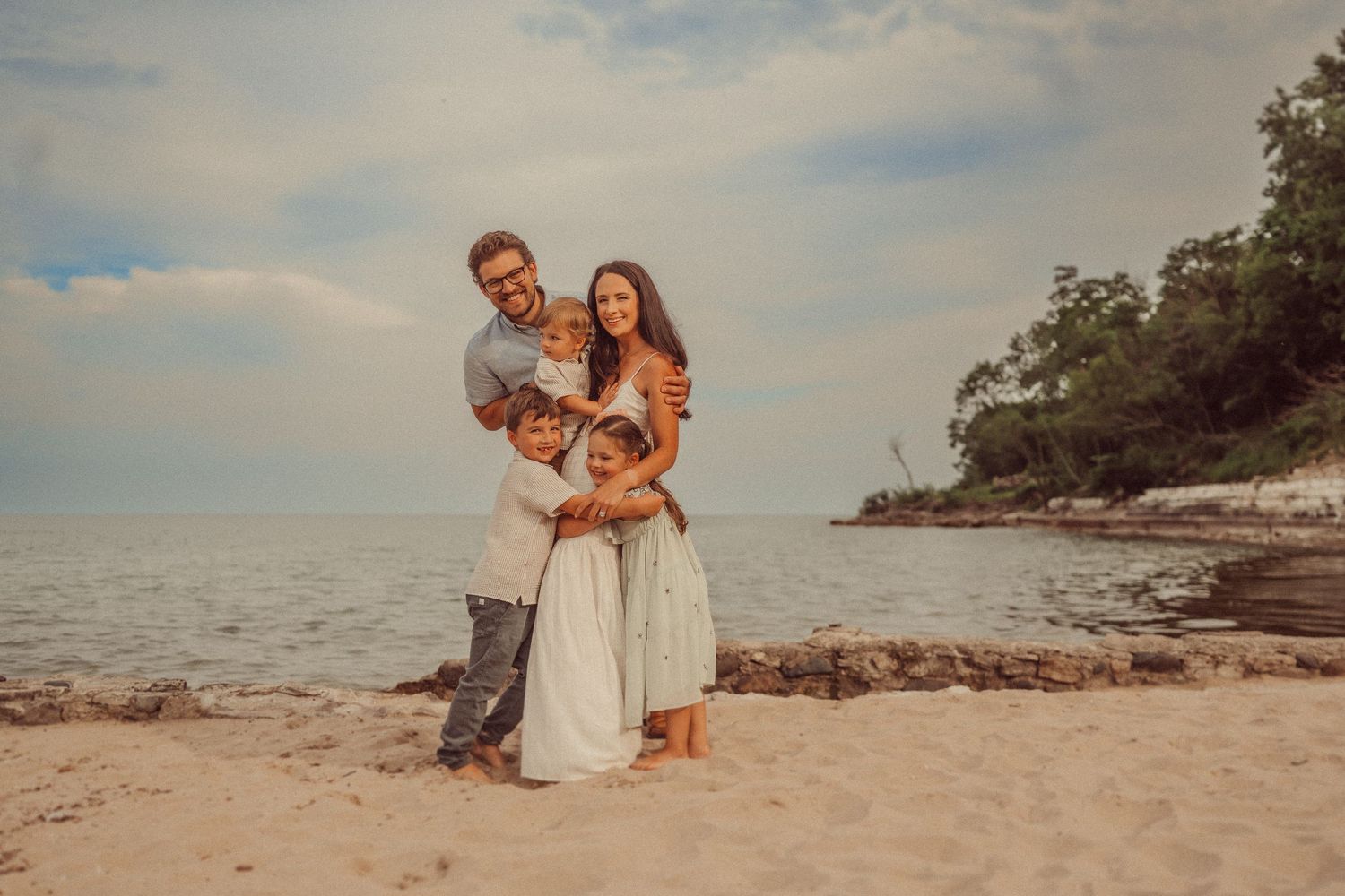 A family shares a warm embrace while posing for photos on a scenic beach.