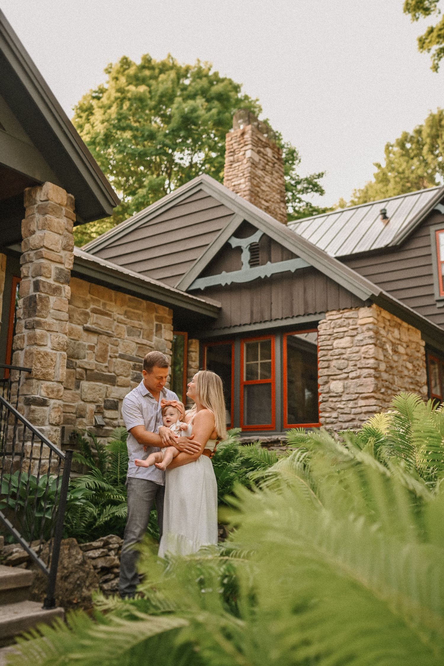 A tender family moment captured outside a rustic stone house surrounded by ferns.