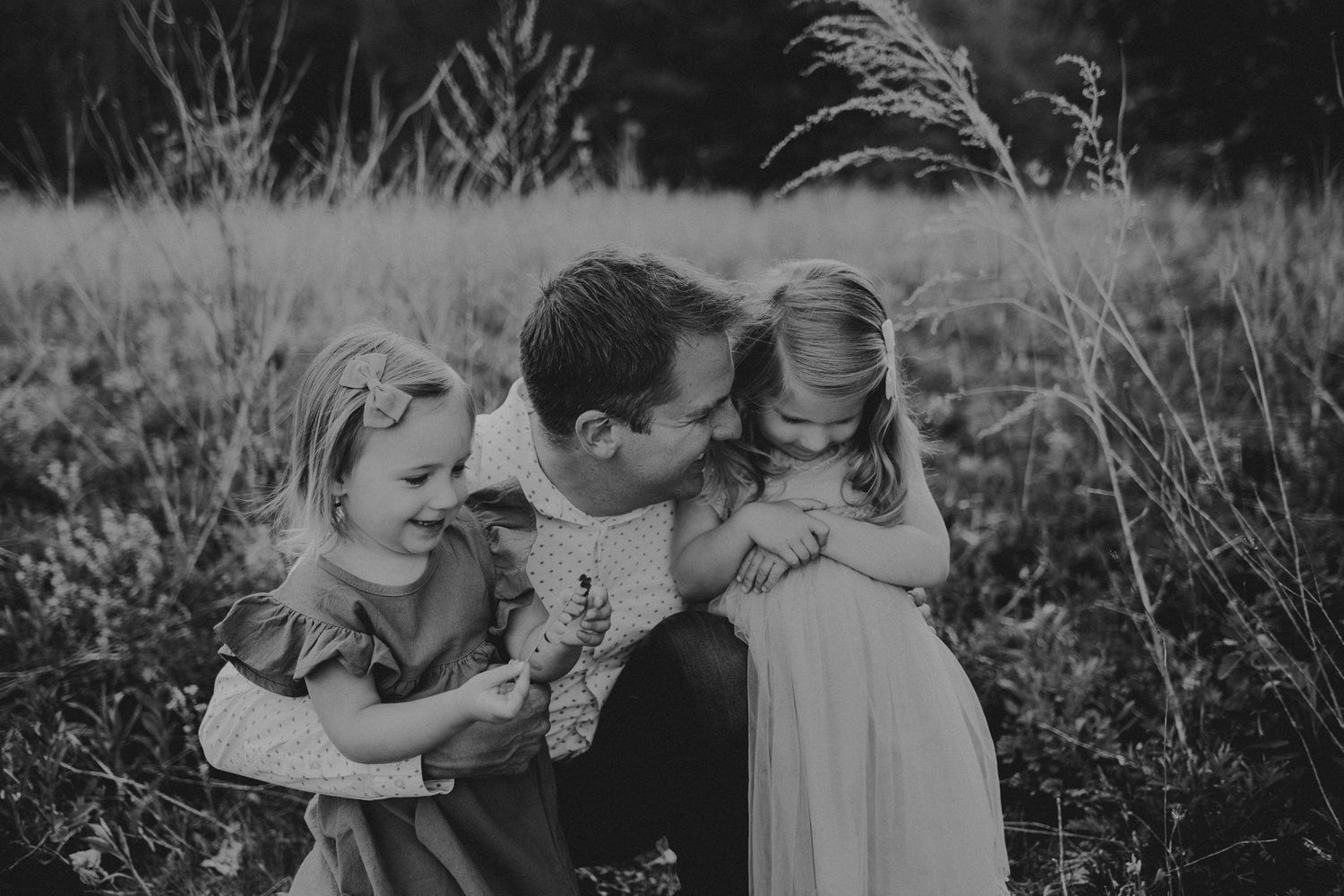 Black and white portrait of tender family moment in a natural field setting.