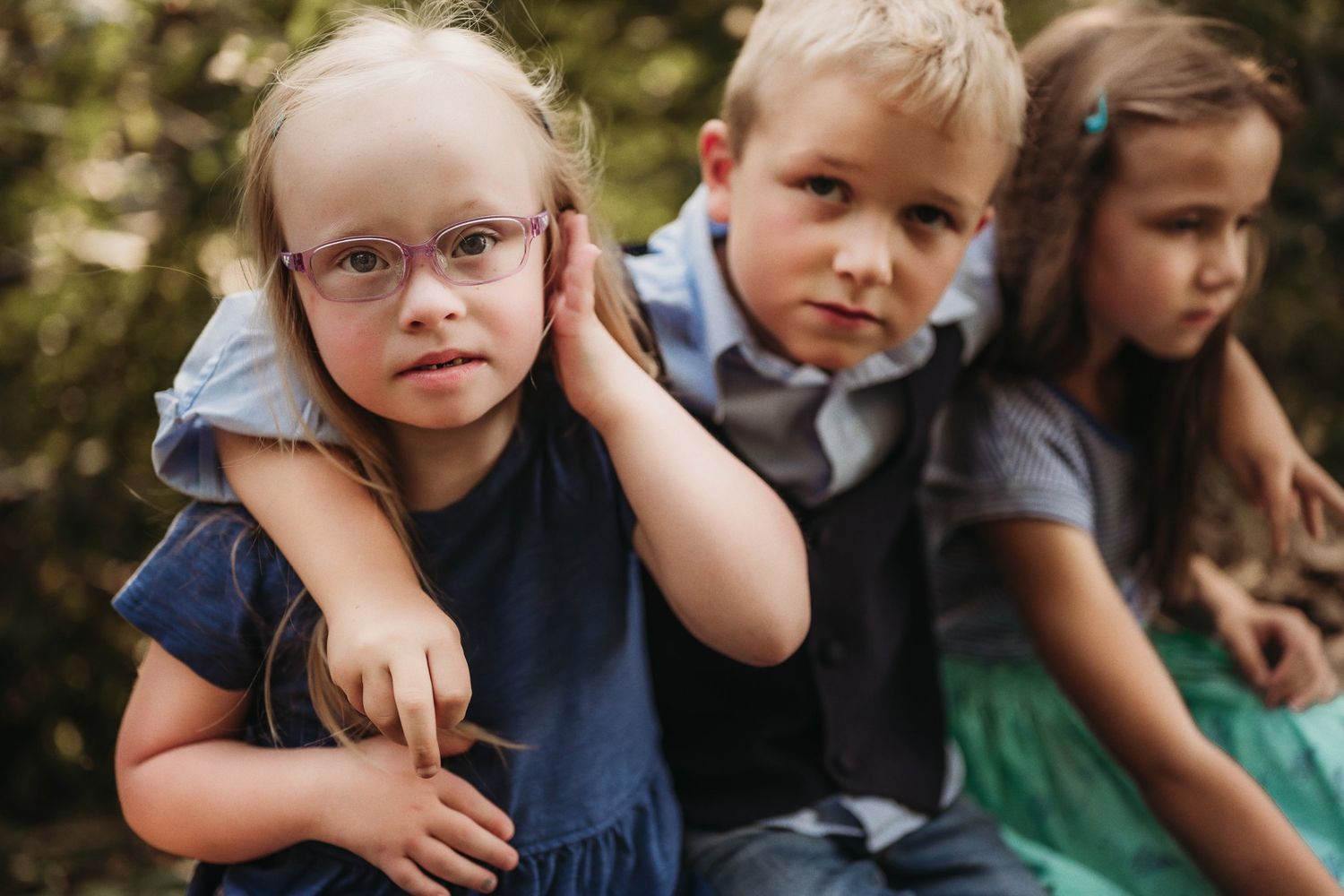 Three children sit together on a log while enjoying time outdoors.