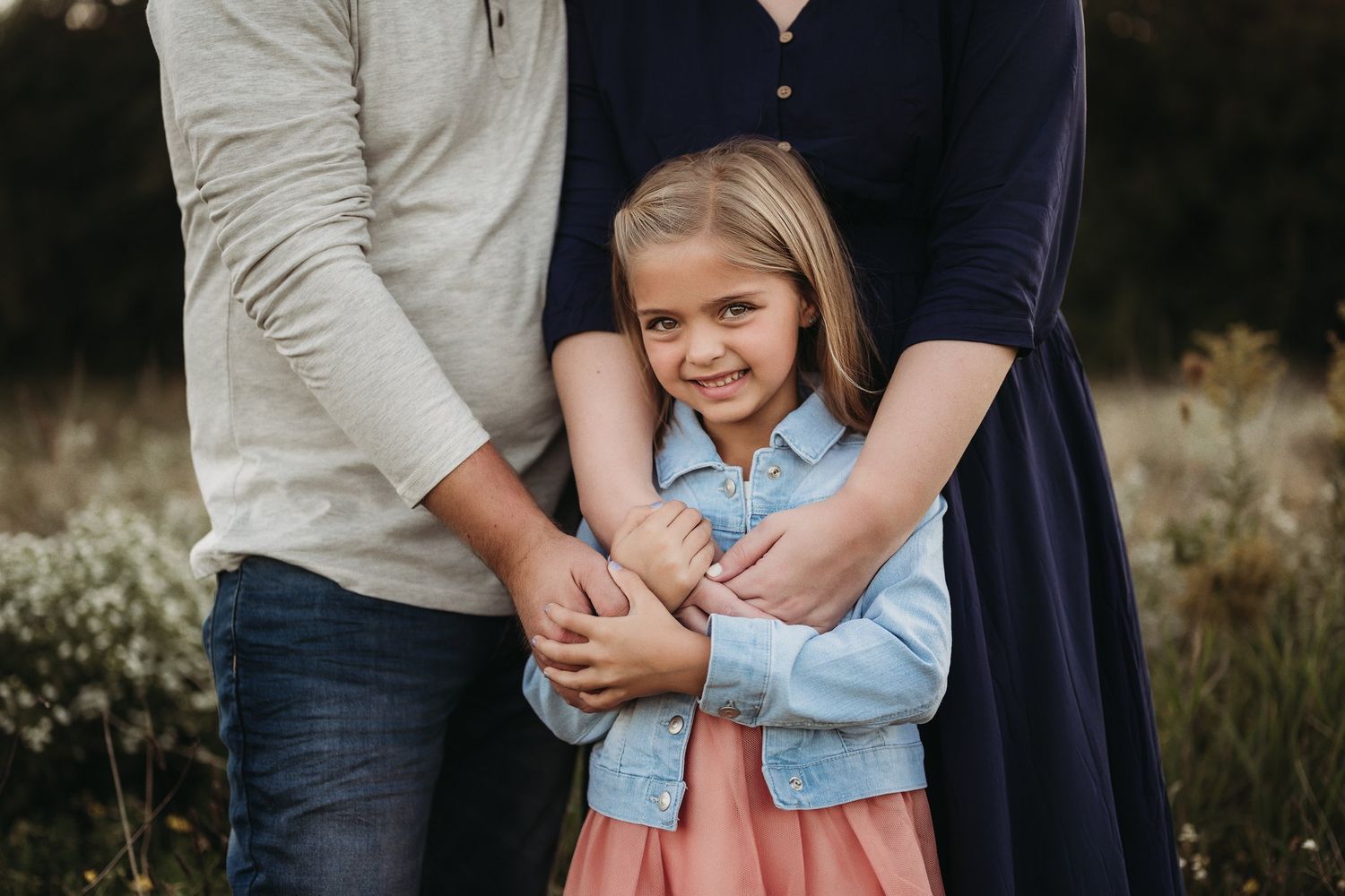 Family portrait showing warm embrace against natural outdoor background.