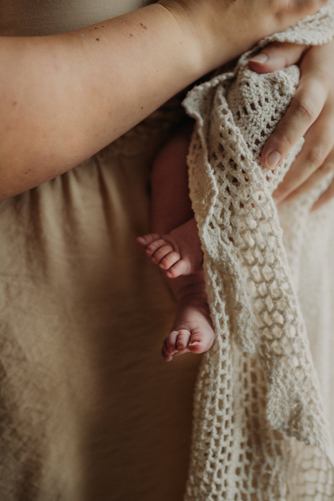 Close-up detail of tiny baby feet peeking through delicate white lace fabric.
