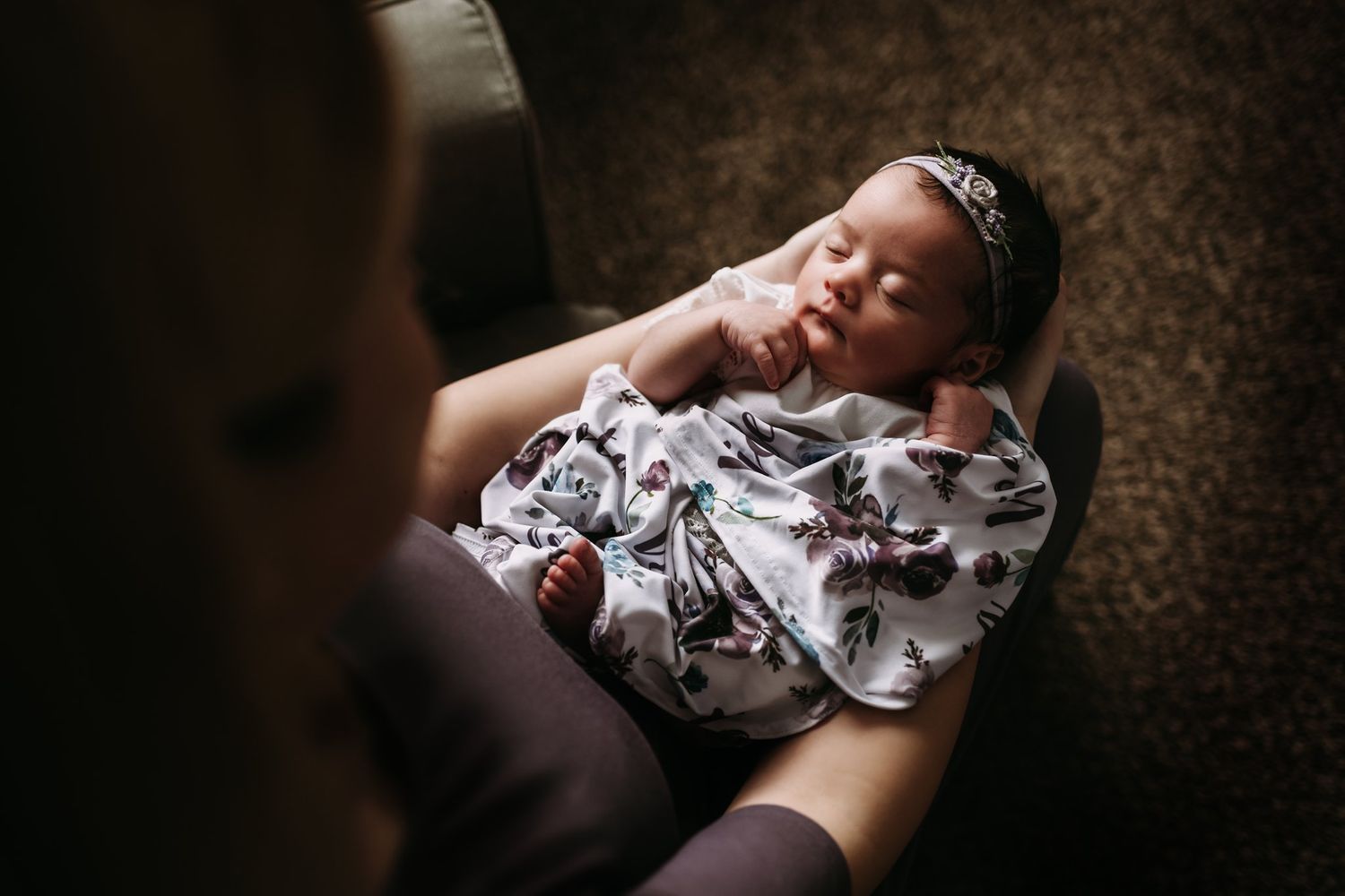 Newborn baby wearing a floral outfit lies peacefully while being gently cradled.
