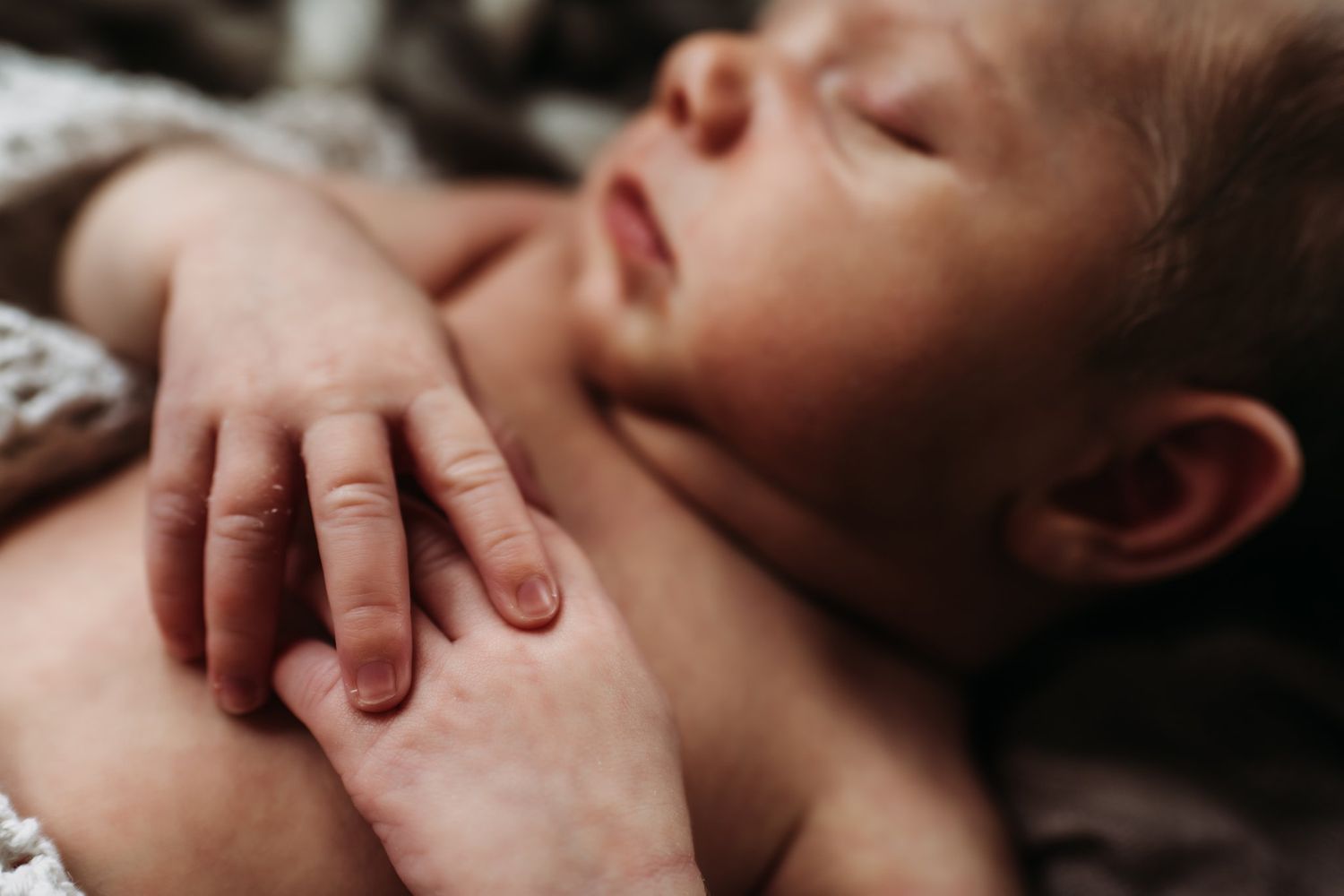 Close-up of a sleeping newborn's hand resting gently on their chest.