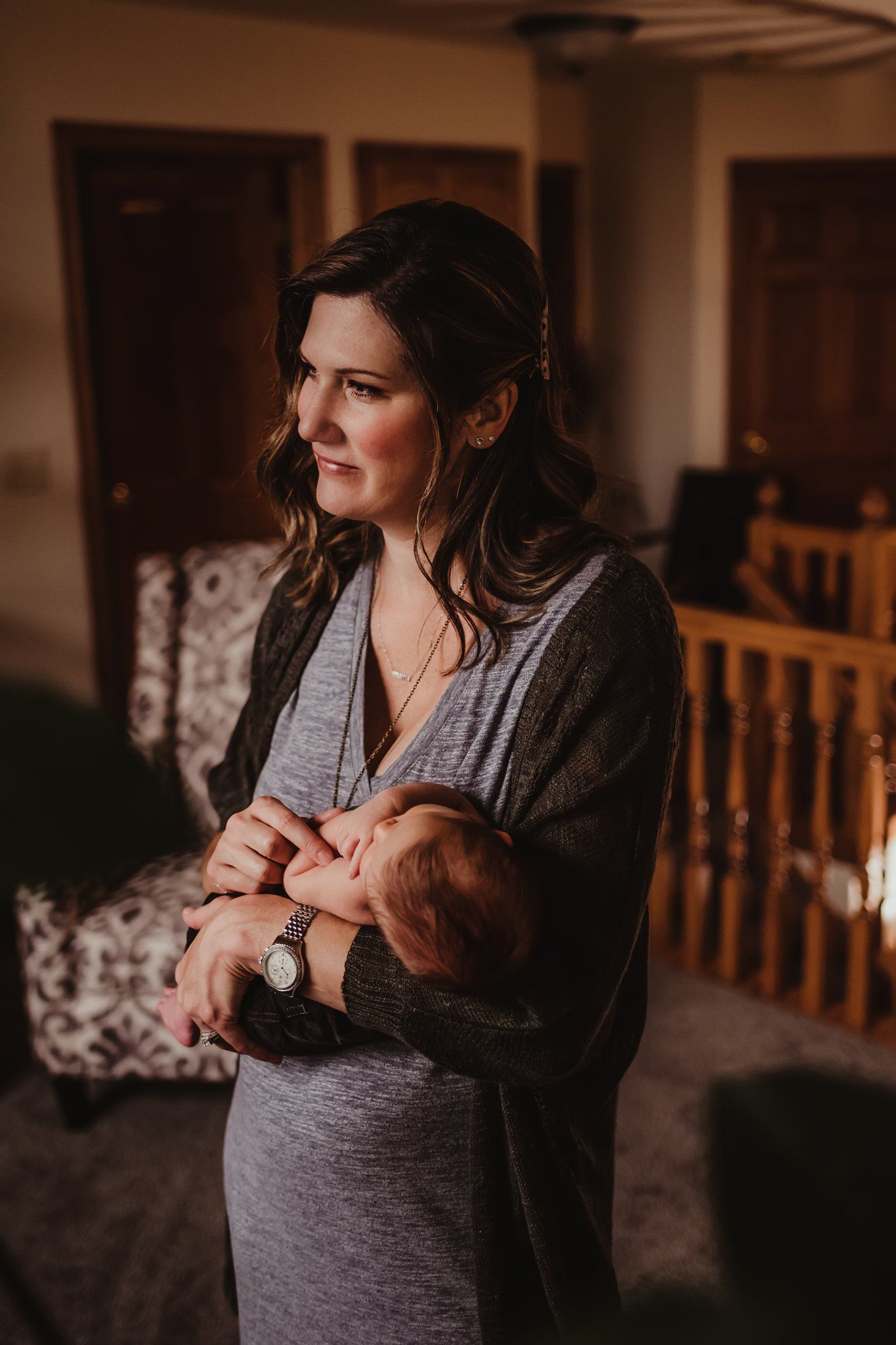 A warm-toned portrait shows a parent holding an infant while standing in a home setting.