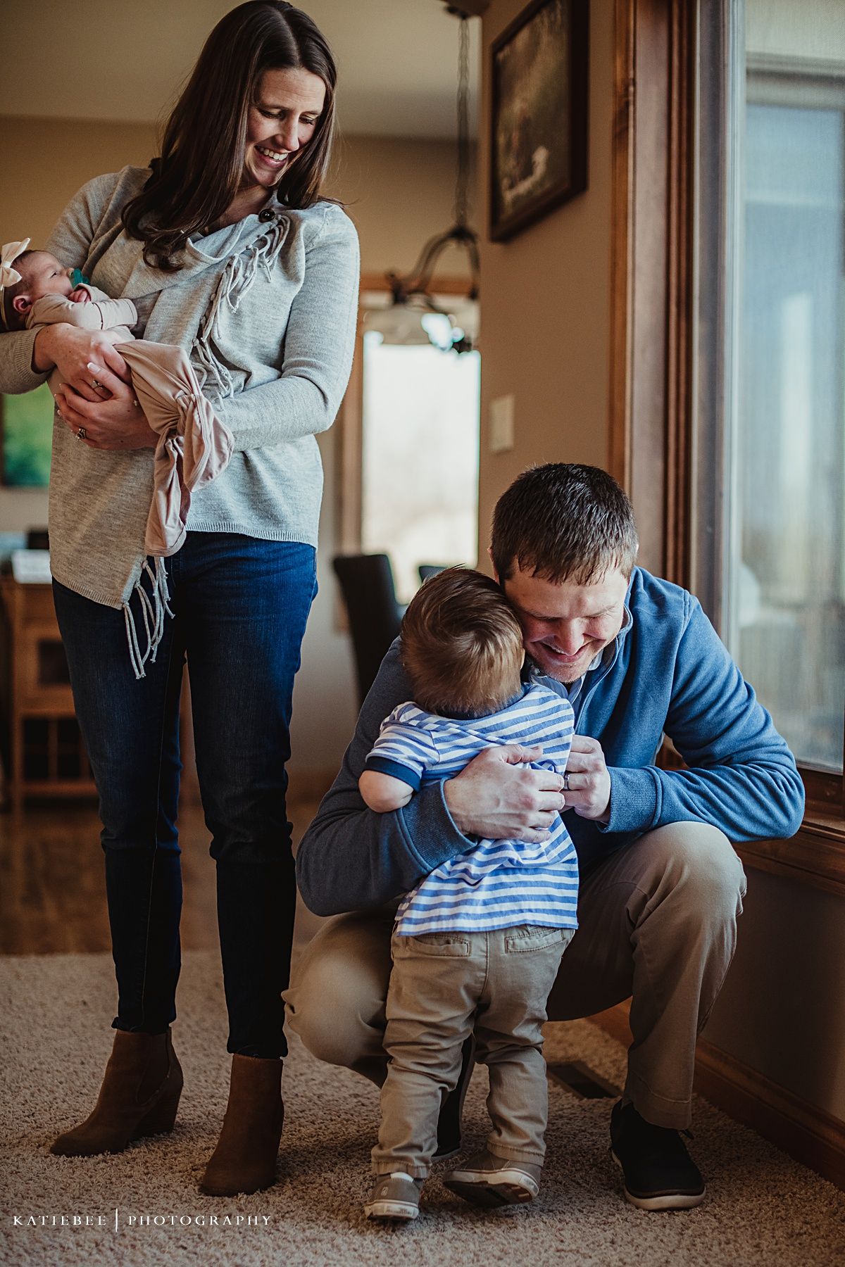 Family gathered in living room with toddler in blue striped shirt during candid lifestyle photography session.