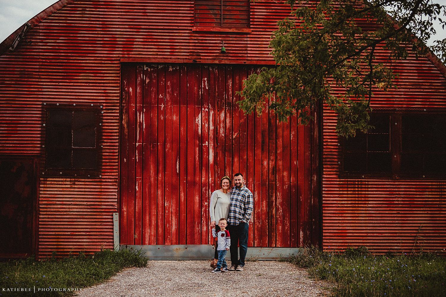 Two people standing in front of a large red barn door during a photo session.
