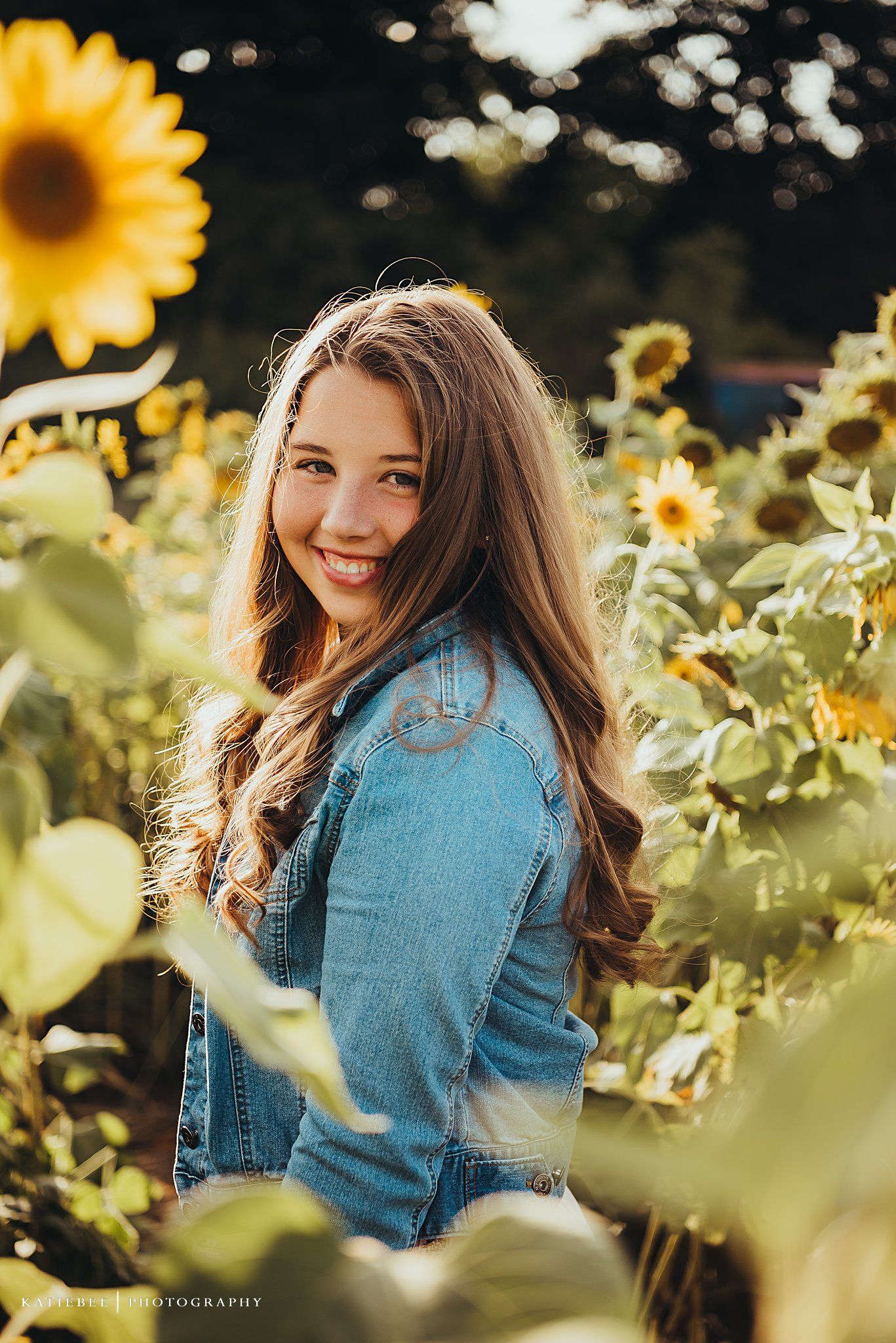 Portrait in a vibrant sunflower field wearing denim jacket with warm sunset lighting.