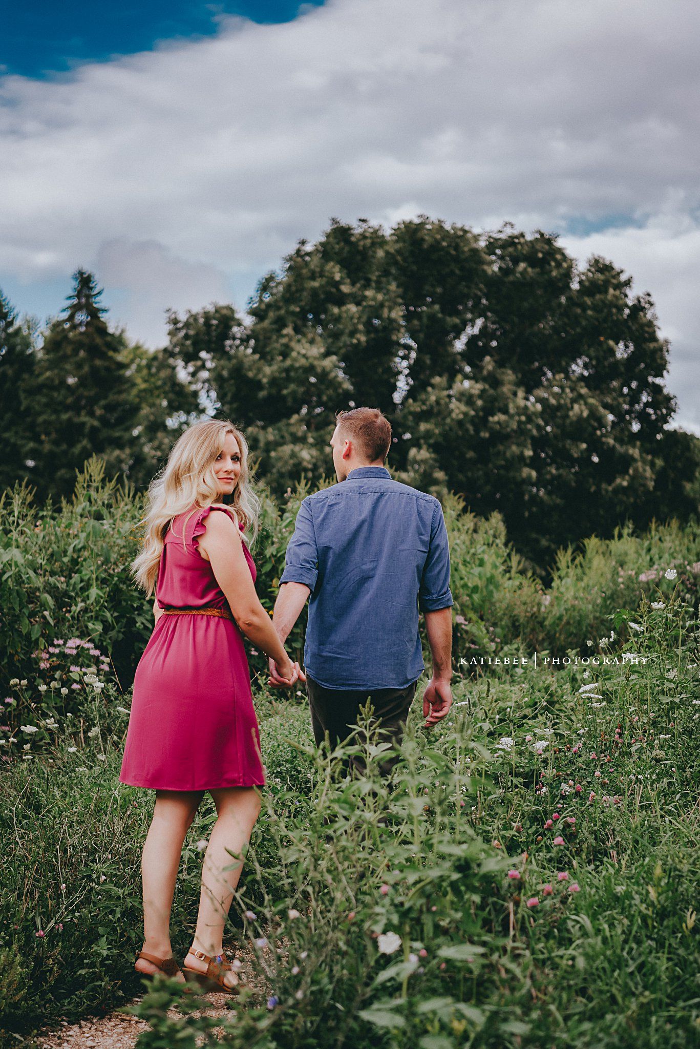 Couple walking hand in hand through a wildflower meadow on a summer day.