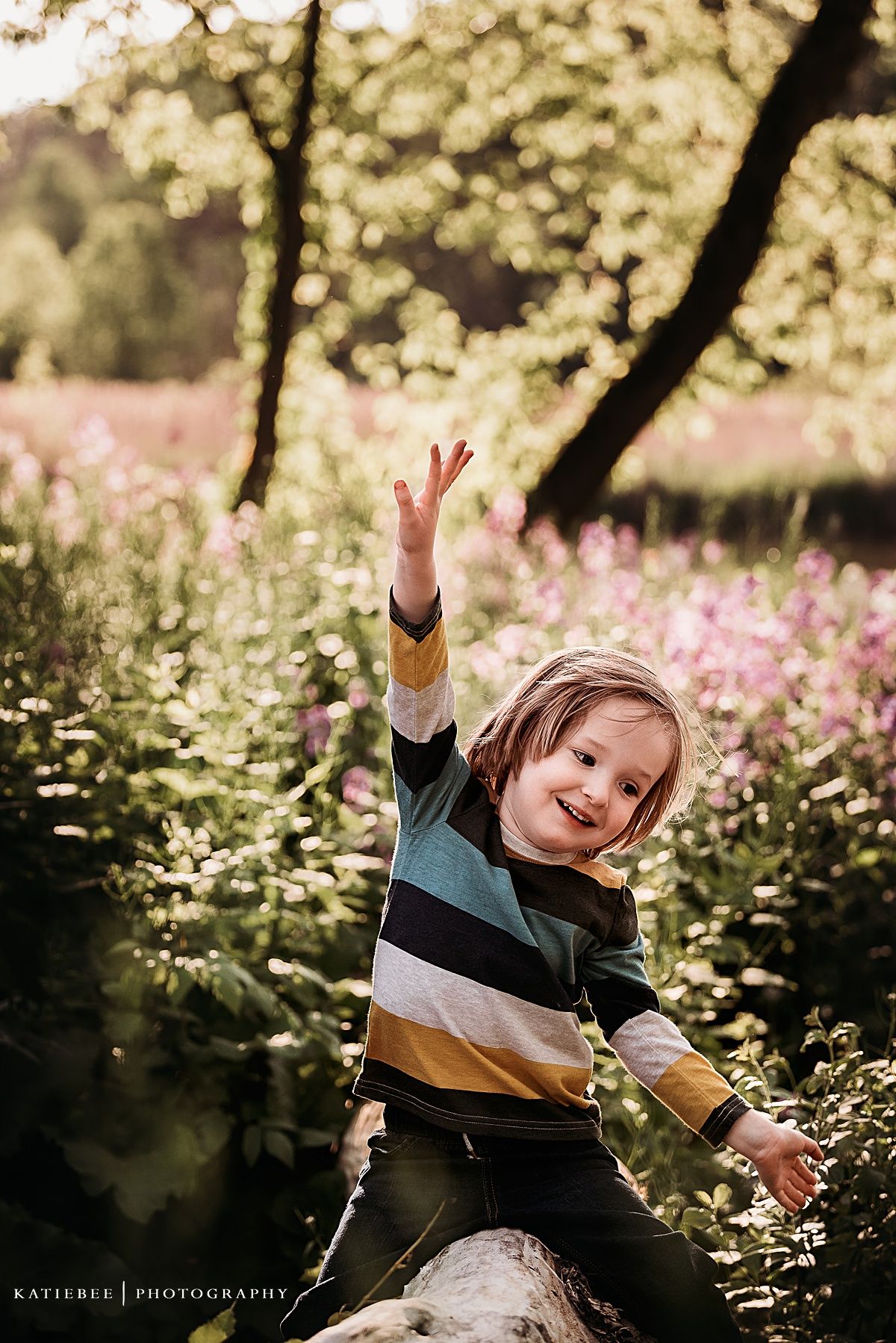 Child in striped sweater poses joyfully among wildflowers during golden hour photography session.