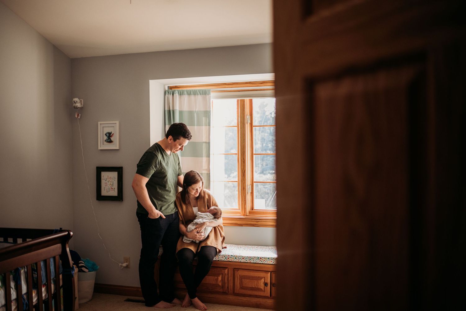 Family gathered by window in nursery room with natural lighting.